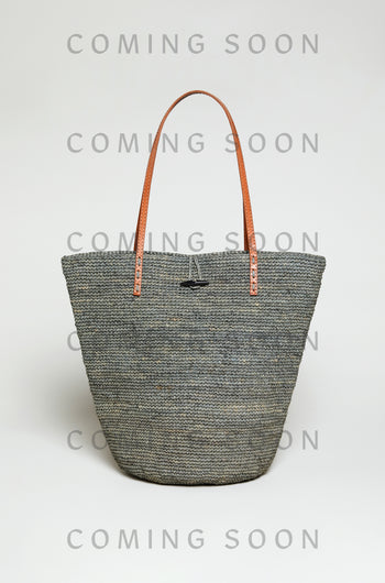The Ilana Raffia Basket, a large woven gray tote with brown leather handles, is shown on a plain light background with "COMING SOON" displayed over the image.