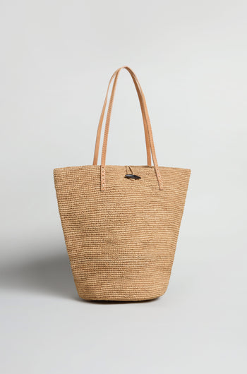 The Ilana Raffia Basket is a woven tote bag with two tan leather handles, shown upright on a plain white background—perfect for adding effortless style to your everyday look.
