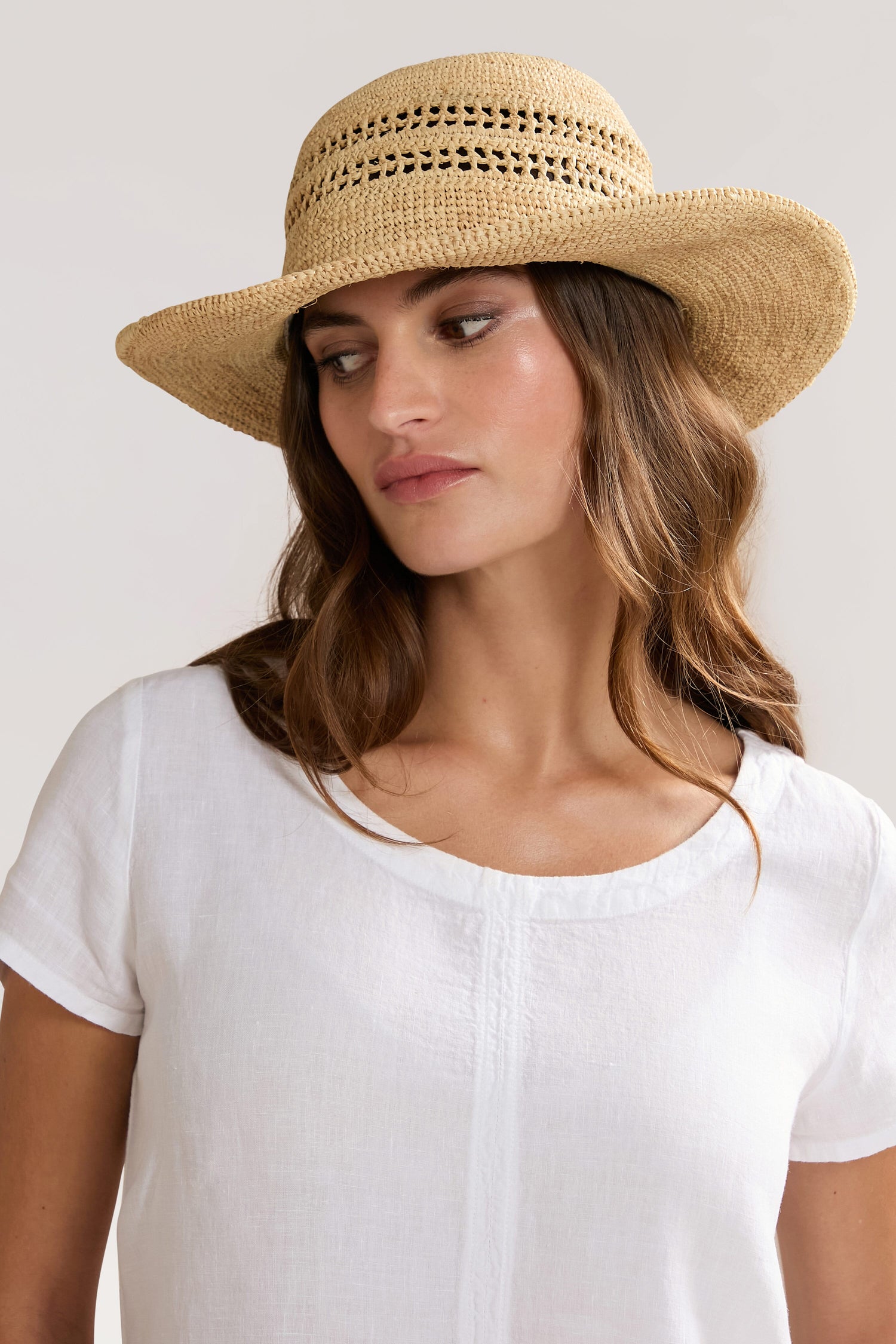 A woman with wavy hair wears a Chapeau Westoloa and a white blouse, looking to the left against a plain background.