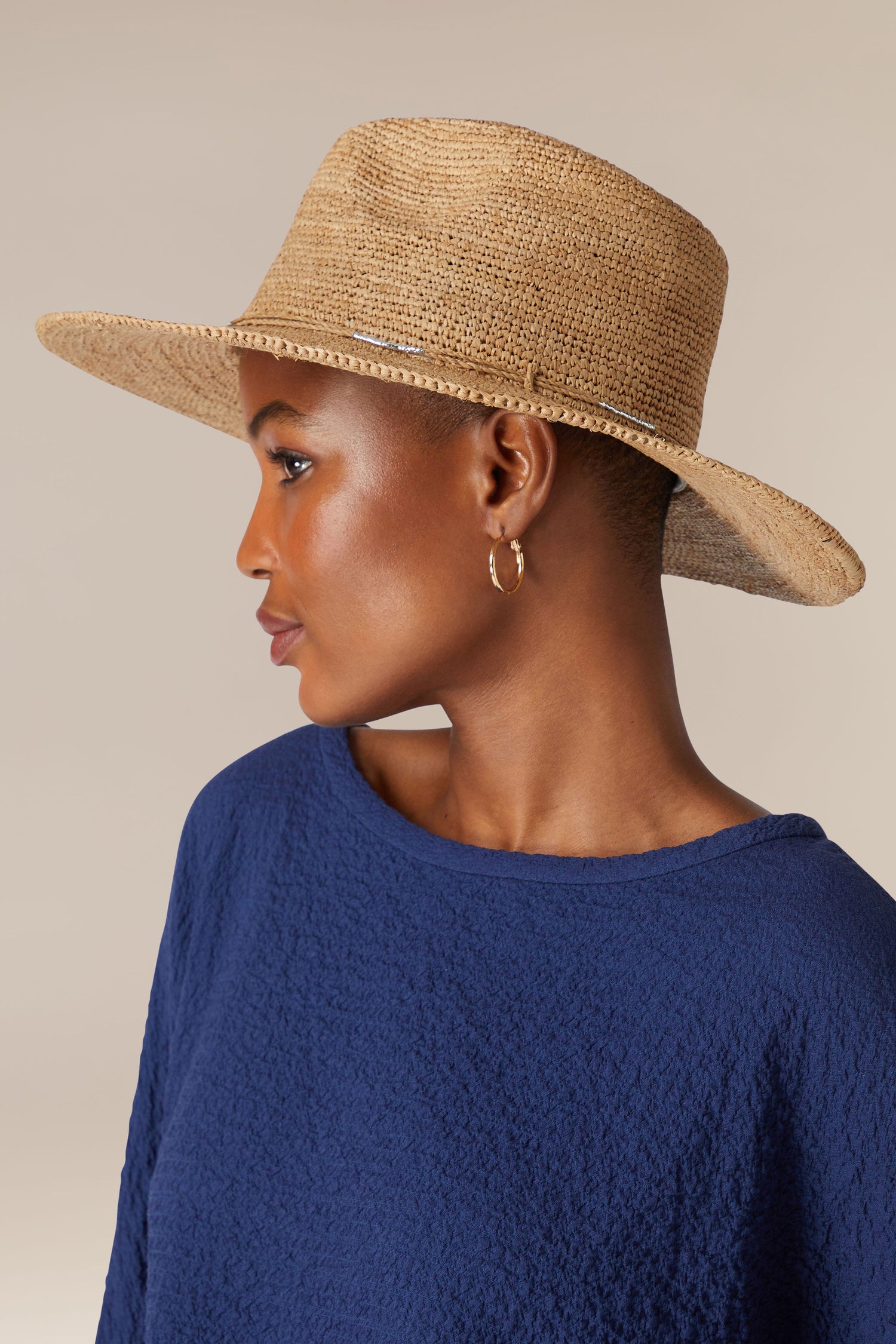 A person wearing a Chapeau Westilux and a blue top, perfect for a summer wardrobe, looks to the side.