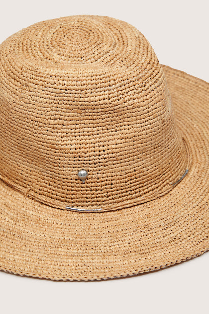 A close-up of a beige woven straw Chapeau Westilux with a wide brim, featuring a small silver button detail on the side, perfect for adding a chic touch to your summer wardrobe.