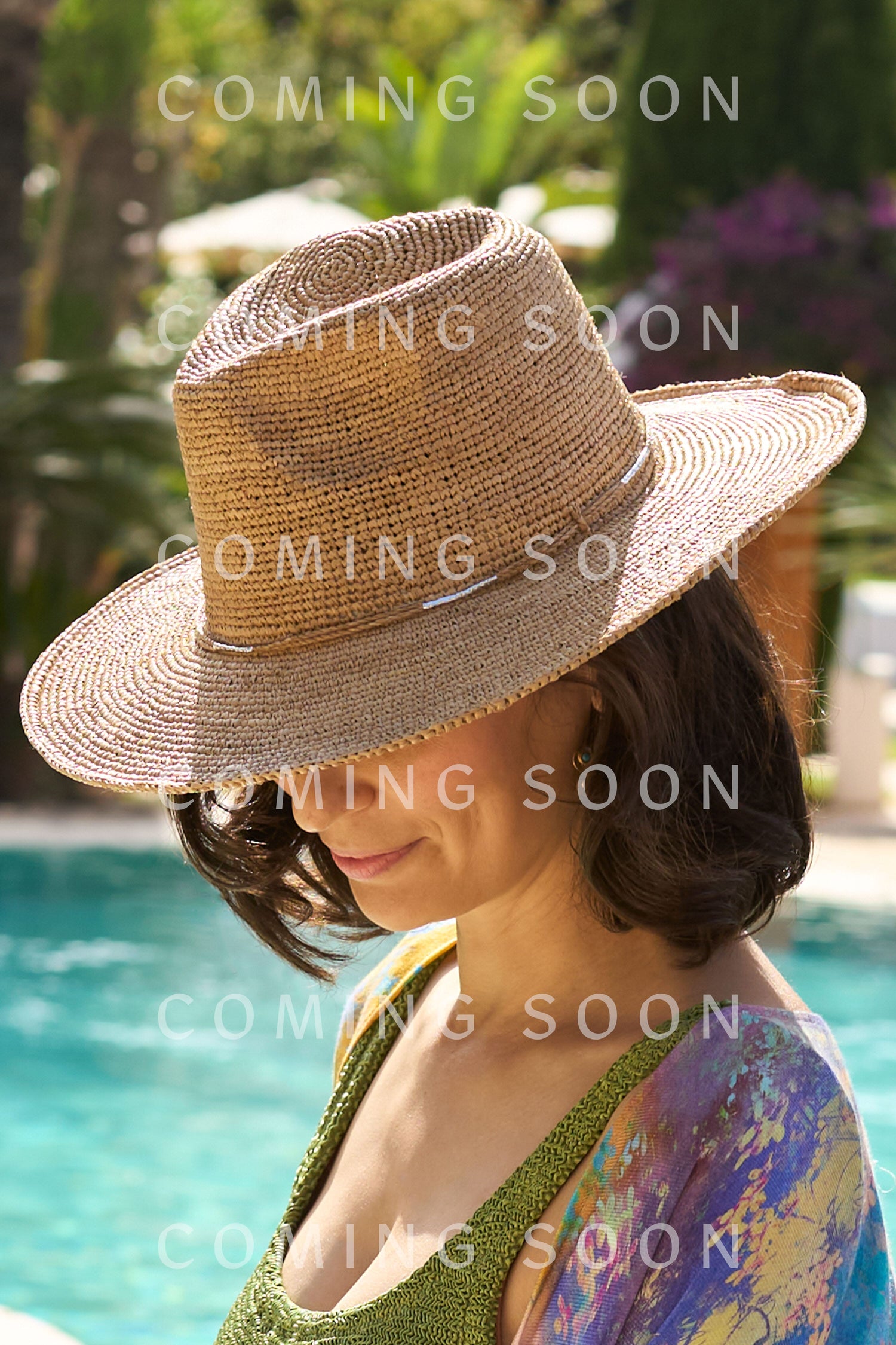 Woman wearing a Chapeau Westilux hat by the poolside with "coming soon" text overlay and model number LVEPAM769-SS24.