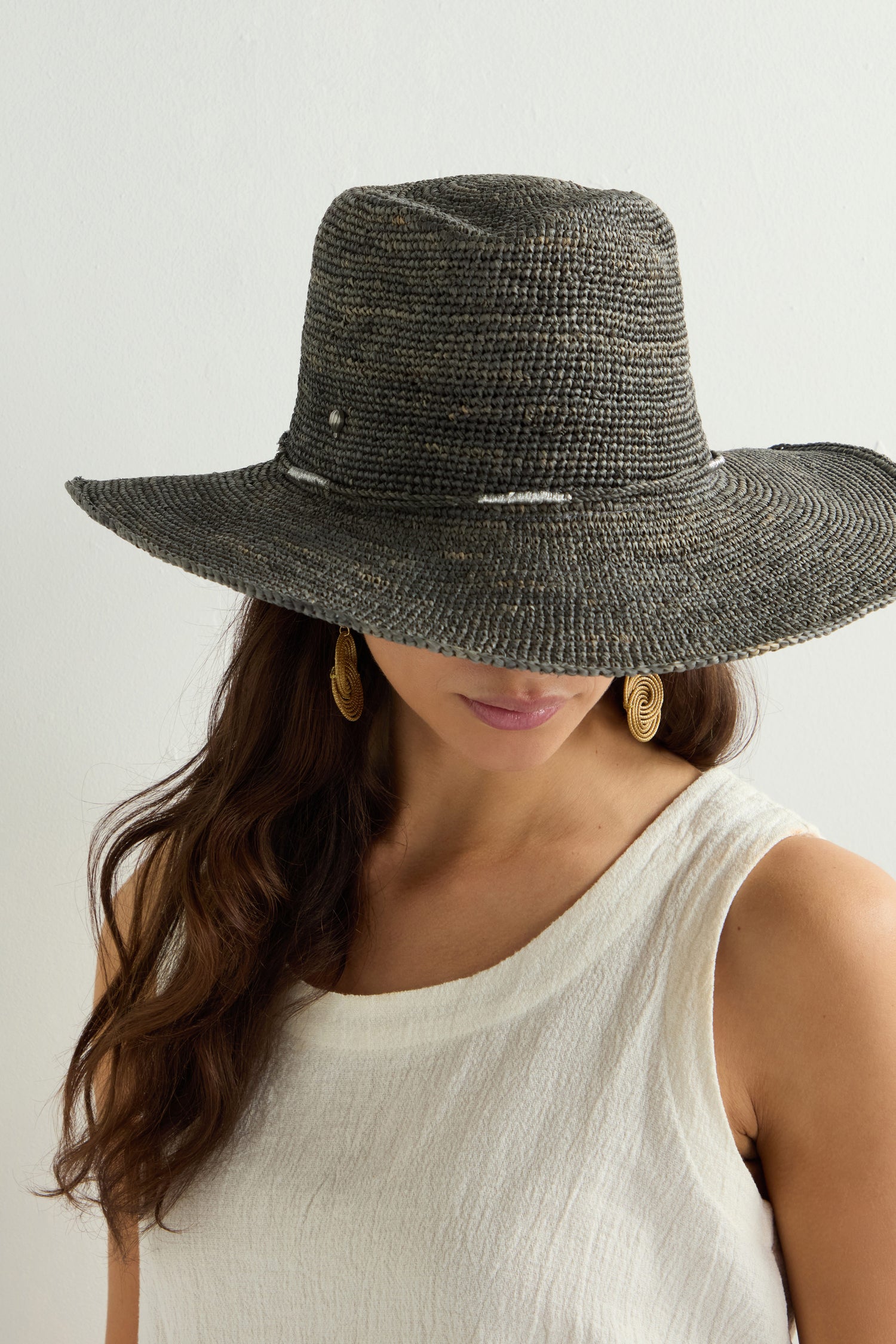 A person with long hair wears a Chapeau Westilux, showcasing its wide-brimmed textured design, paired with a sleeveless white top against a plain background—a perfect summer wardrobe addition.