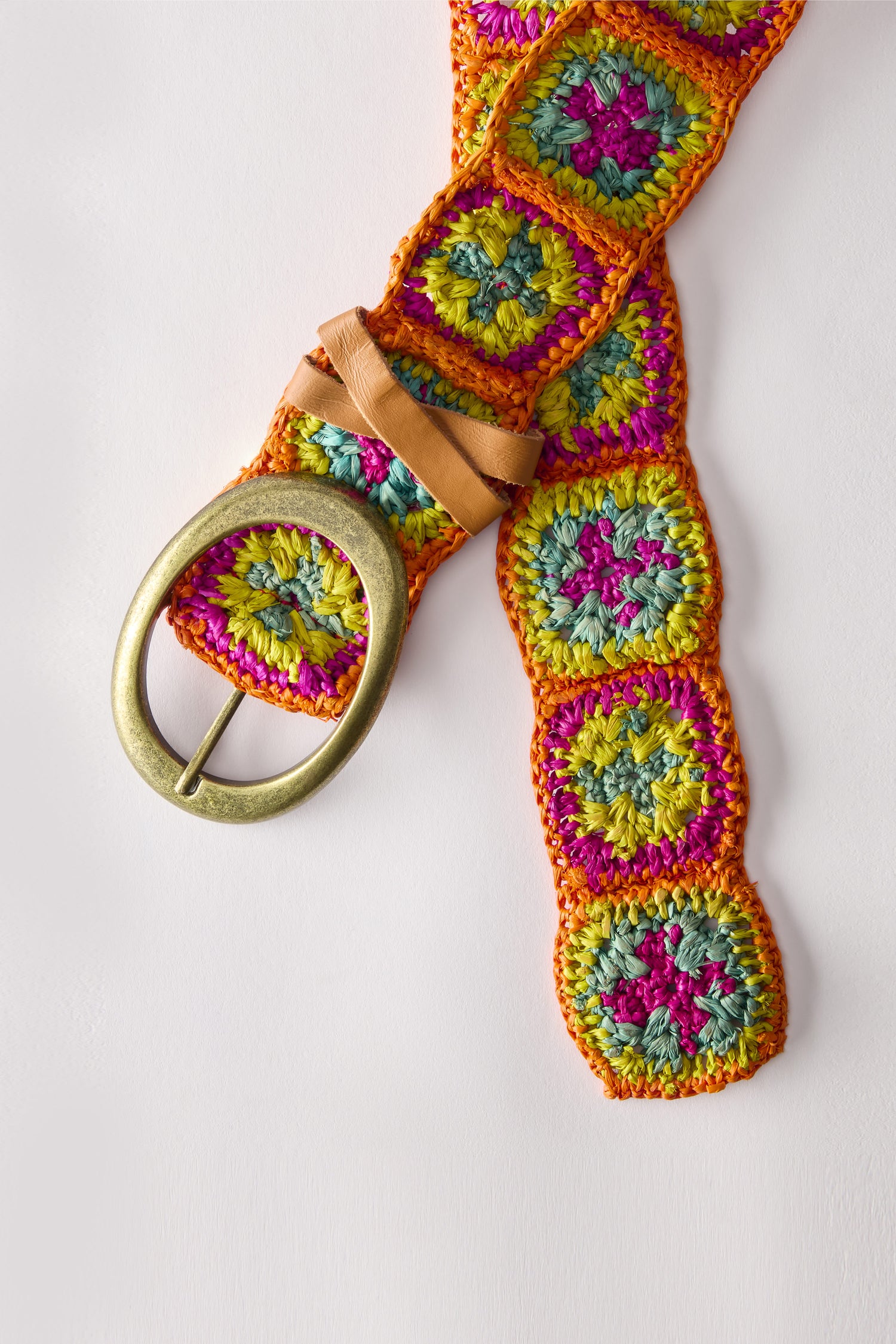 The Rainbow Cinzoa Raffia Belt, adorned with vibrant orange, pink, green, and yellow squares and a round brass buckle, rests on a white background. This boho-chic accessory effortlessly complements any outfit.