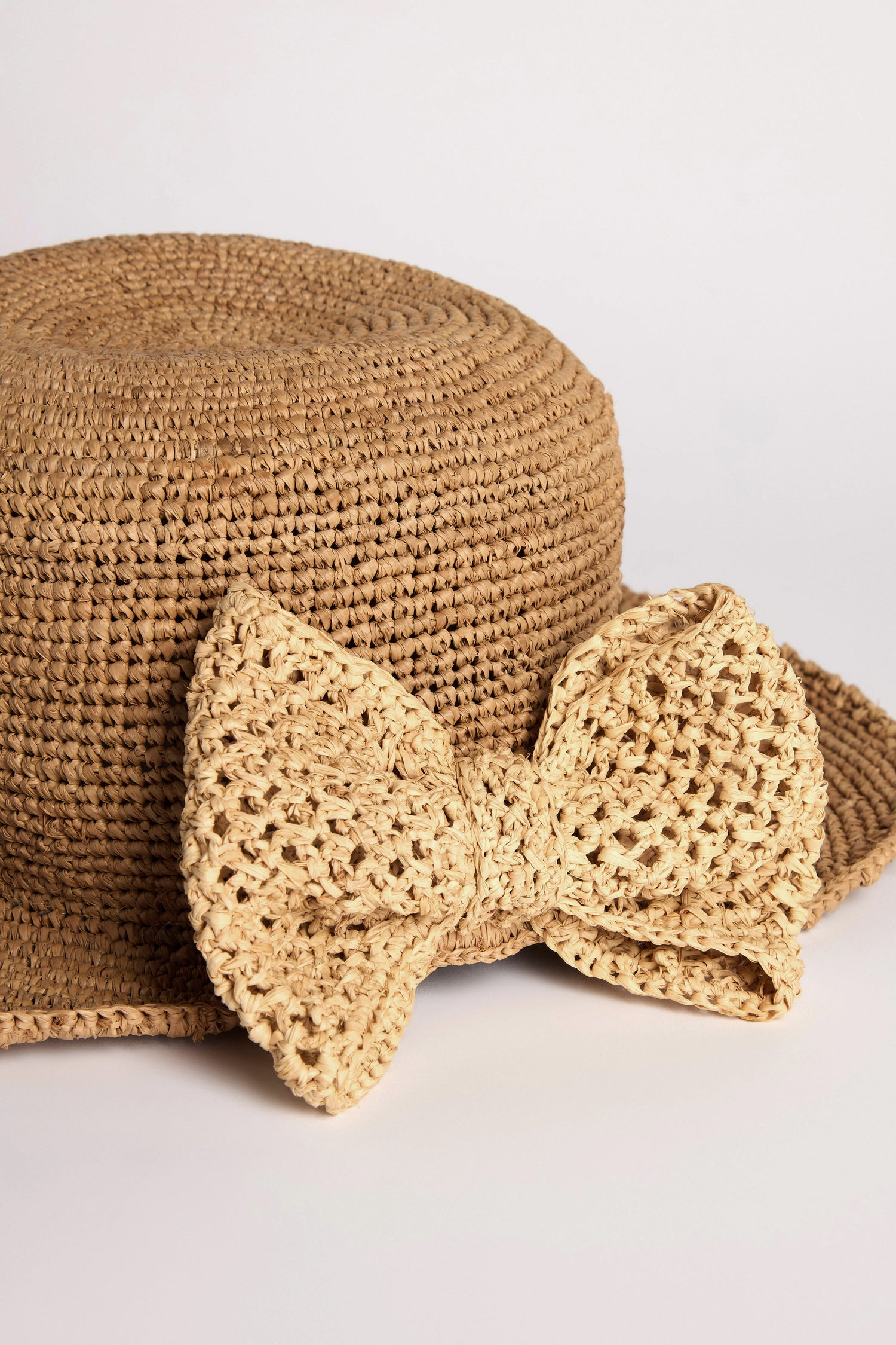 The Chapeau Noloa is a straw wide-brim hat elegantly featuring a large decorative side bow, embodying the essence of summer style against a plain white backdrop.