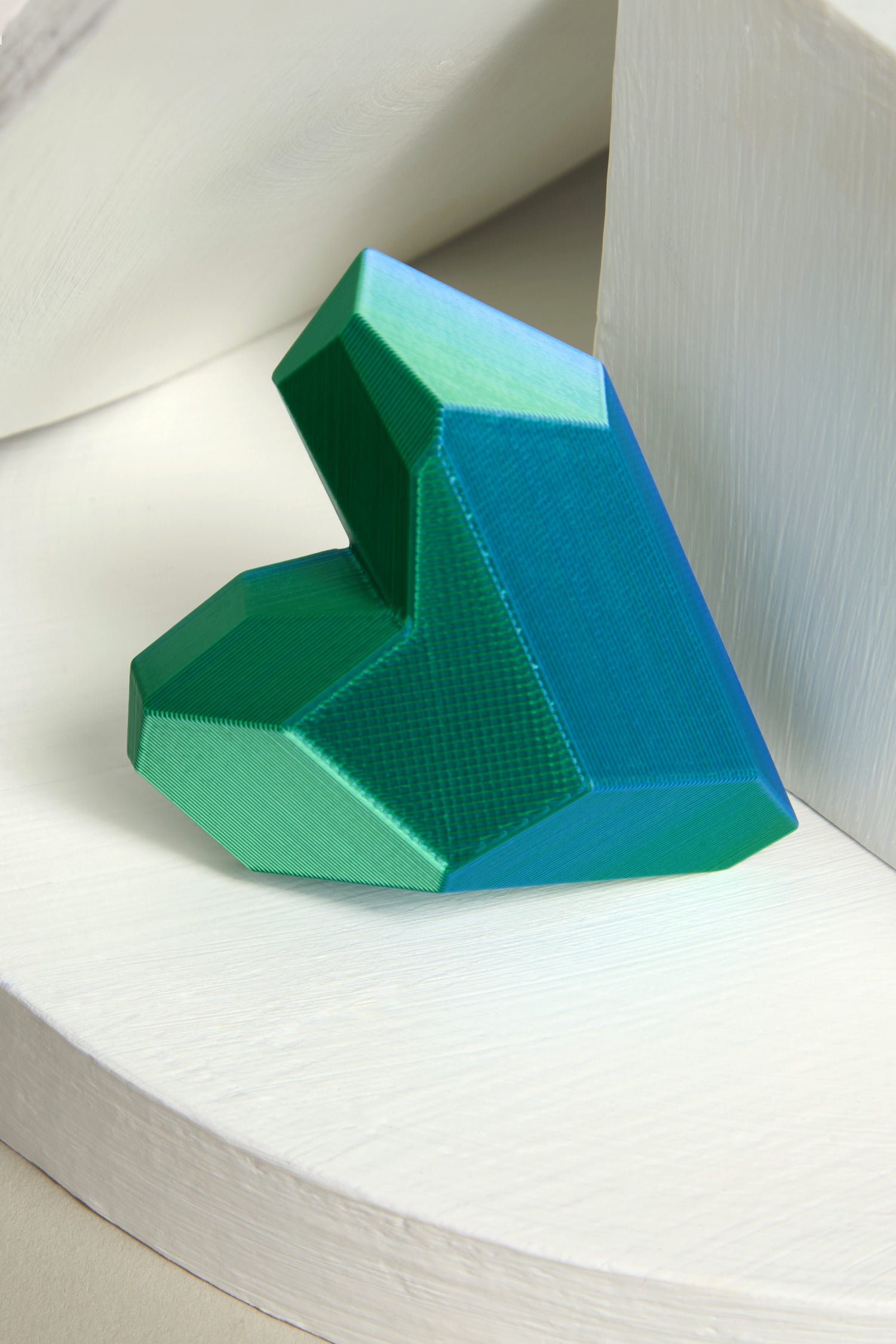 Resting on a white surface is the 3D Printed Heart Brooch, designed with geometric patterns in shades of green and blue. This modern accessory showcases cutting-edge 3D printing techniques, seamlessly merging art with technology.