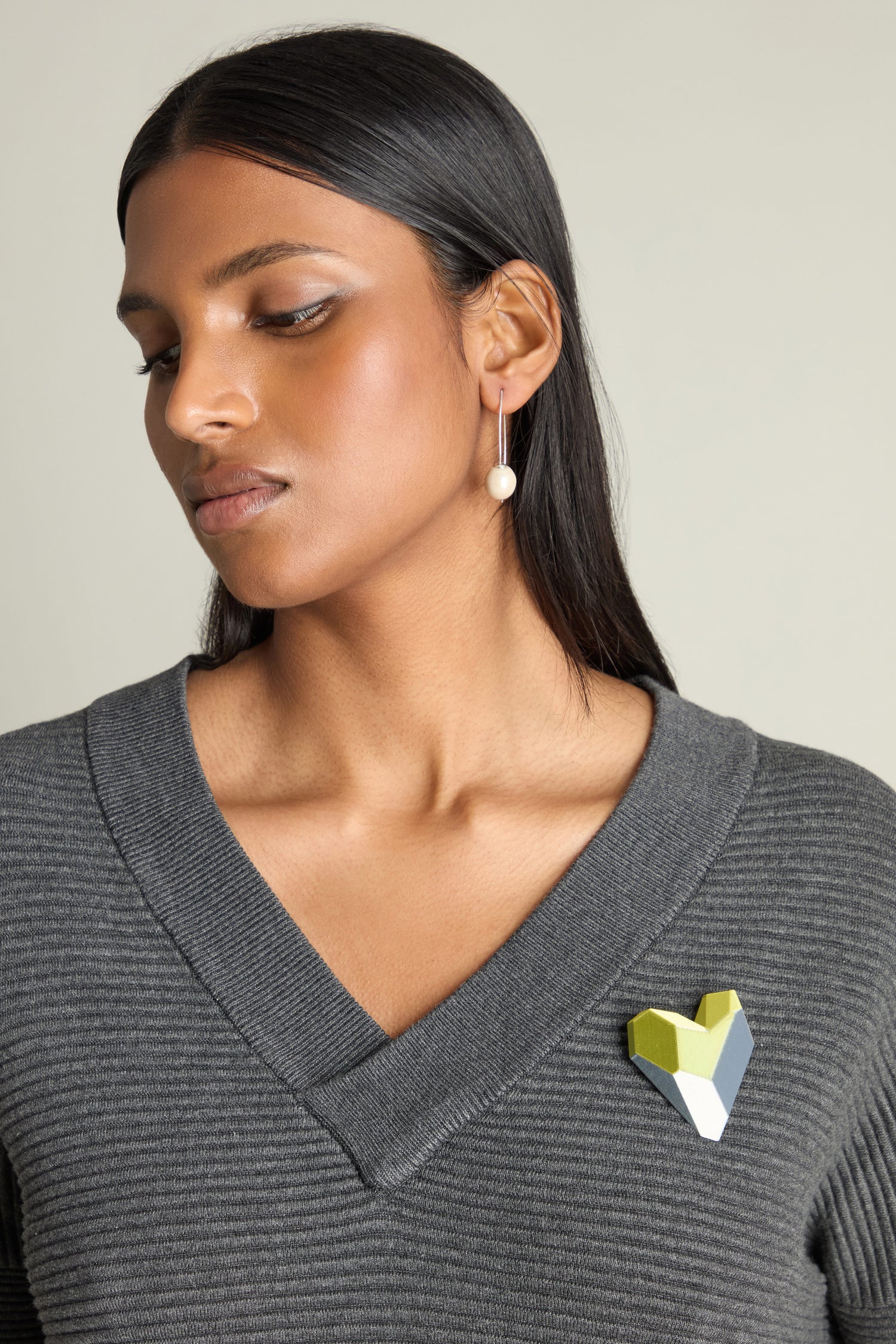 A woman with long dark hair wears a gray V-neck sweater, a 3D Printed Heart Brooch, and a pearl earring.