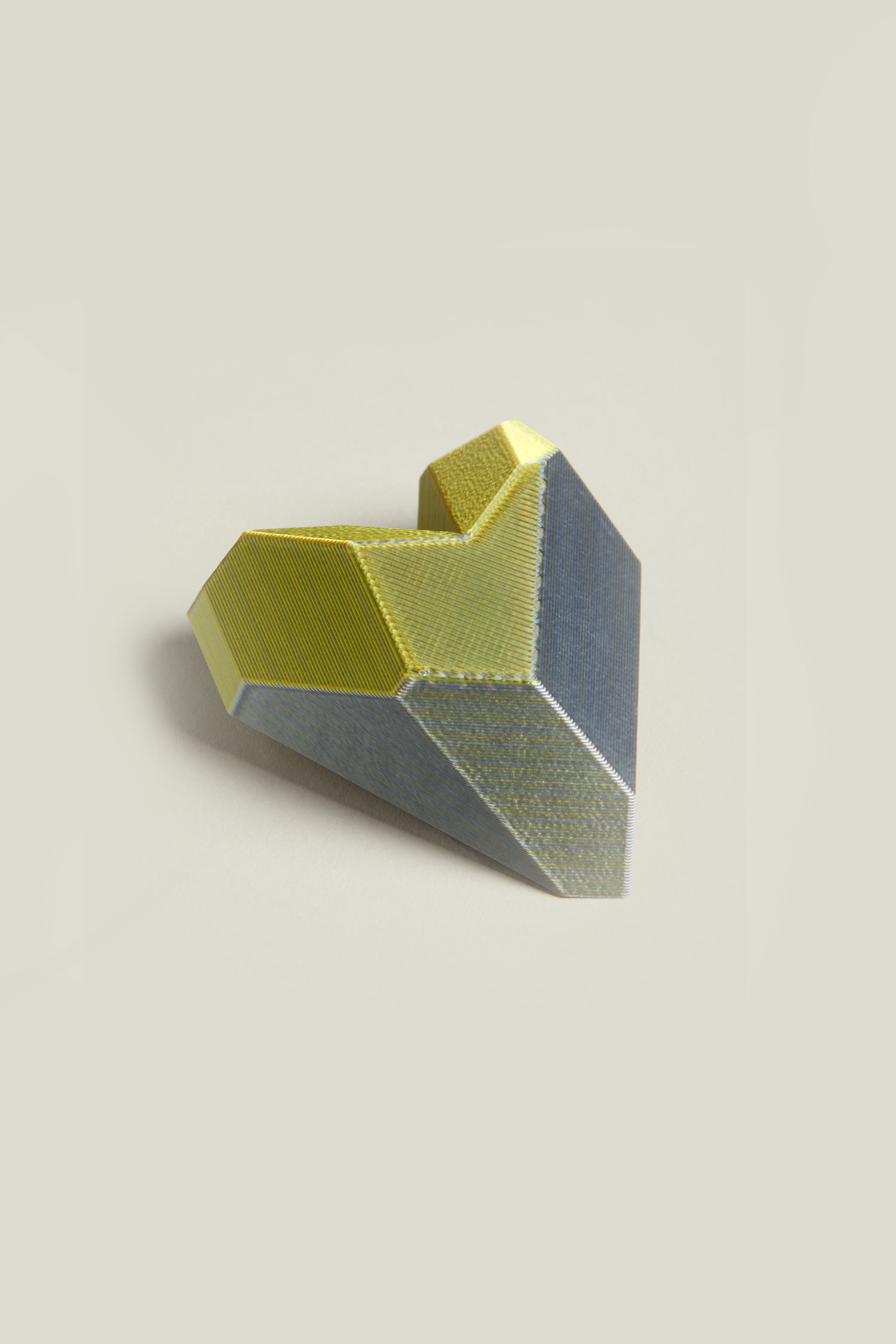 The 3D Printed Heart Brooch is a faceted, heart-shaped accessory showcasing metallic gold and gray tones on a light gray background, embodying the essence of modern design through advanced 3D printing techniques.