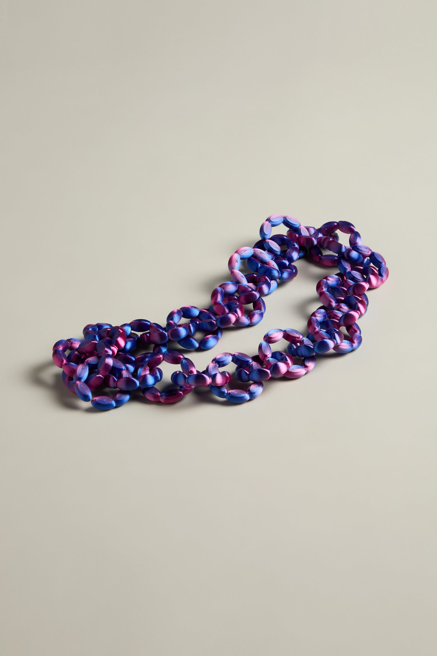 The 3D Printed Links Necklace from Maison 203 is elegantly displayed on a plain light gray background, highlighting its ultra-lightweight design. This multicolored acrylic piece boasts shades of purple, blue, and pink with intricately designed links that bring a modern twist to its vibrant allure.