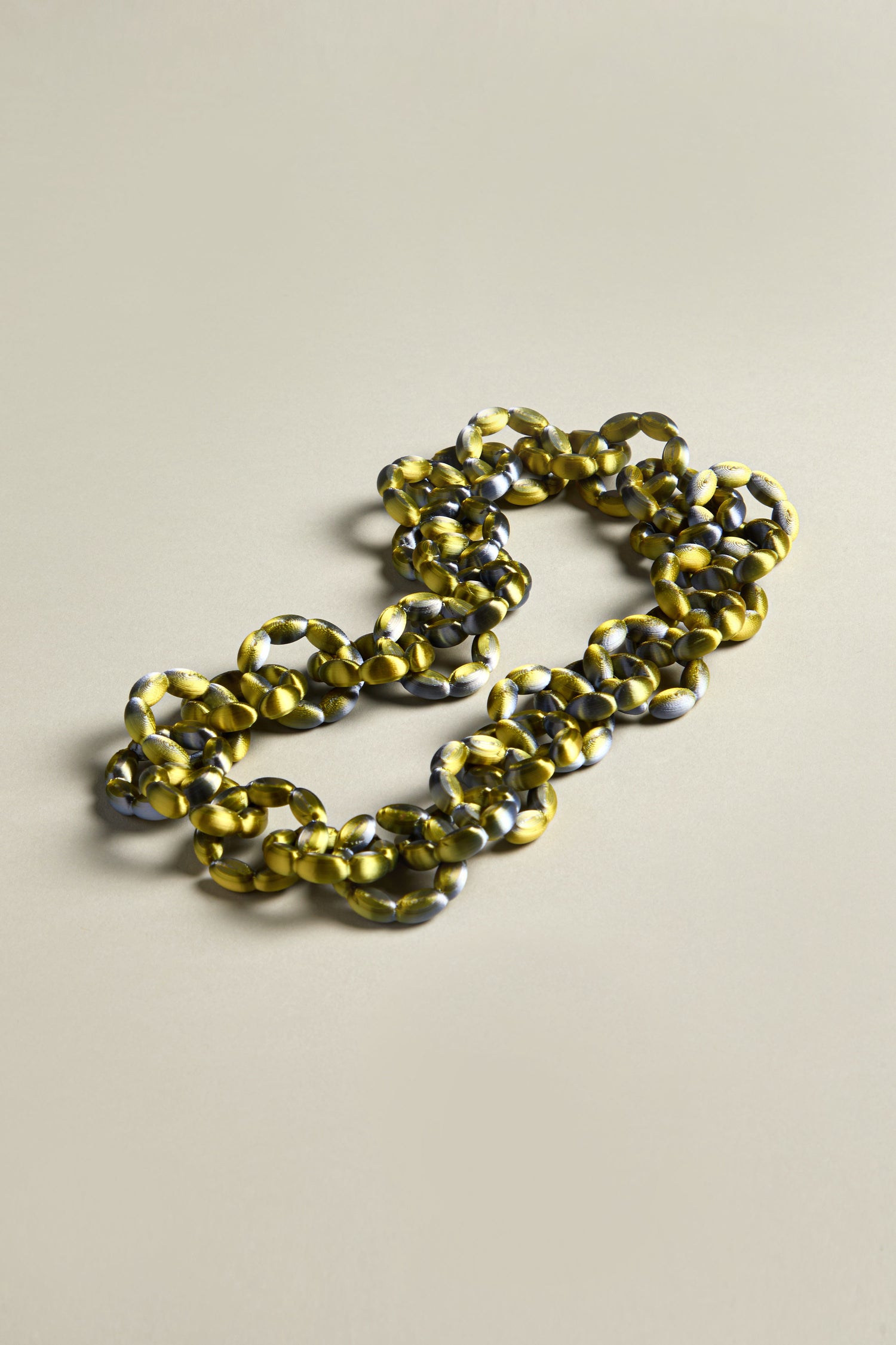 The 3D Printed Links Necklace from Maison 203 showcases a chunky, multicolored chain with a marbled yellow and gray pattern, offering an ultra-lightweight design that elegantly rests on a neutral background.