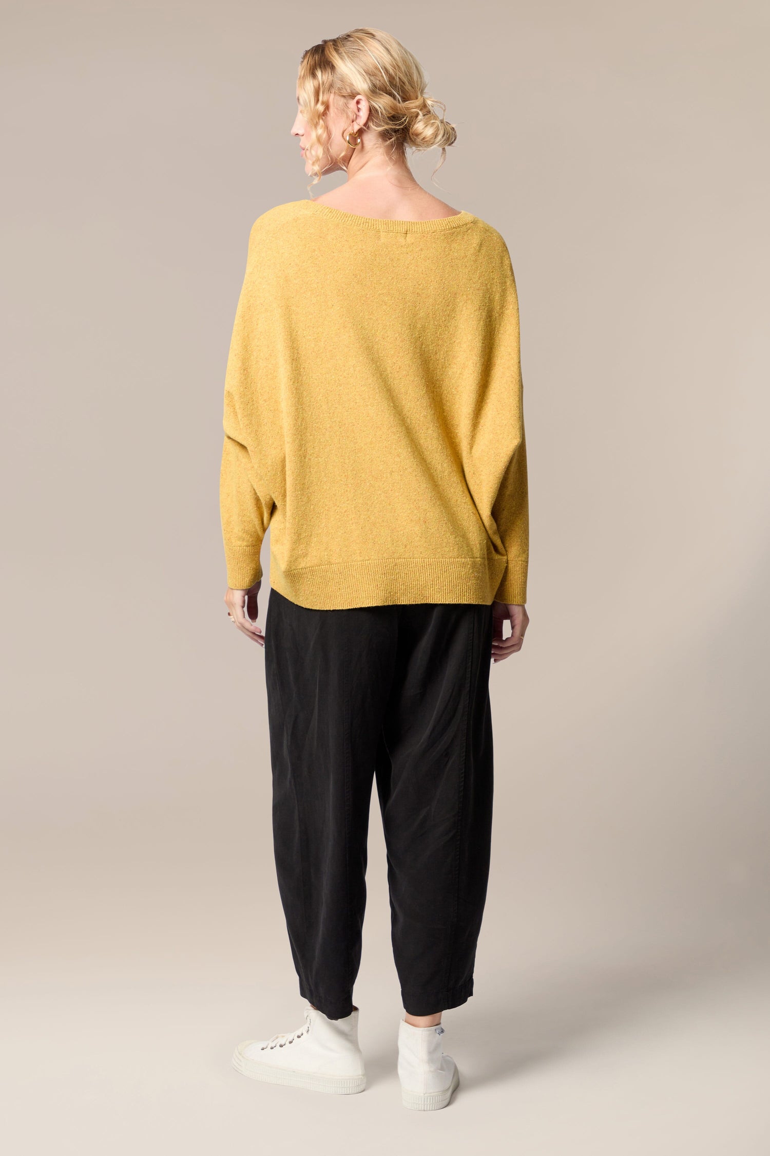 The back view of a woman wearing a Granit Scoop Knit sweater and black trousers, exuding movement and an effortlessly stylish ethos.