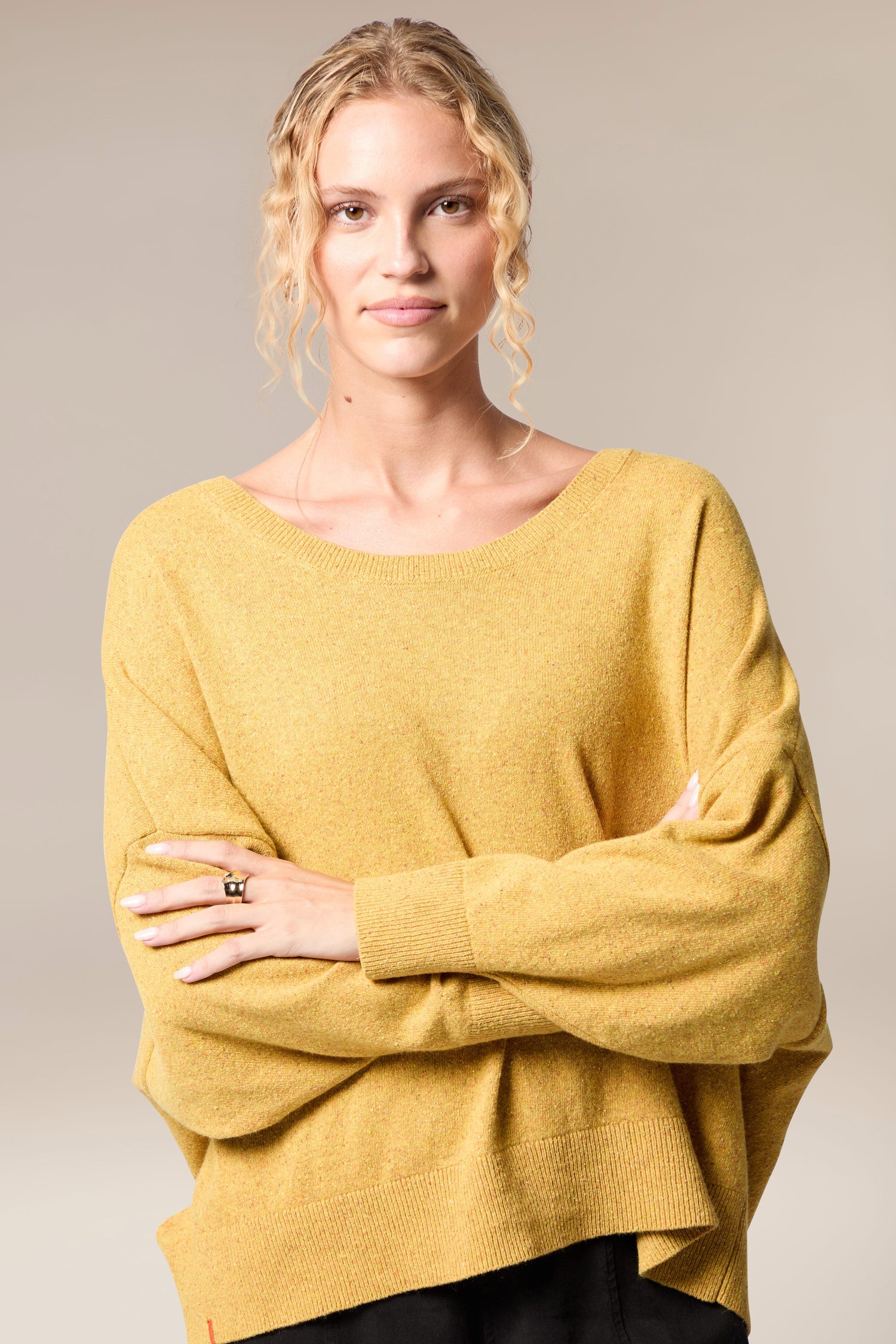 A woman with a vibrant yellow Granit Scoop Knit sweater showcasing her unique knitting craftsmanship while elegantly moving in her ensemble of black pants.