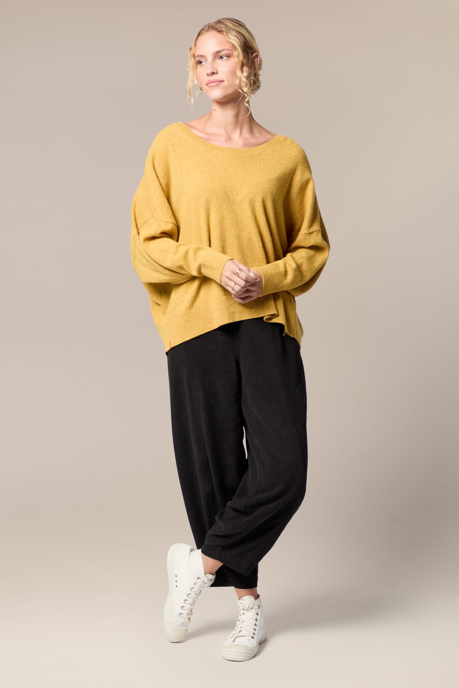 A woman wearing a Granit Scoop Knit sweater and black trousers, exuding an aura of warmth and movement.