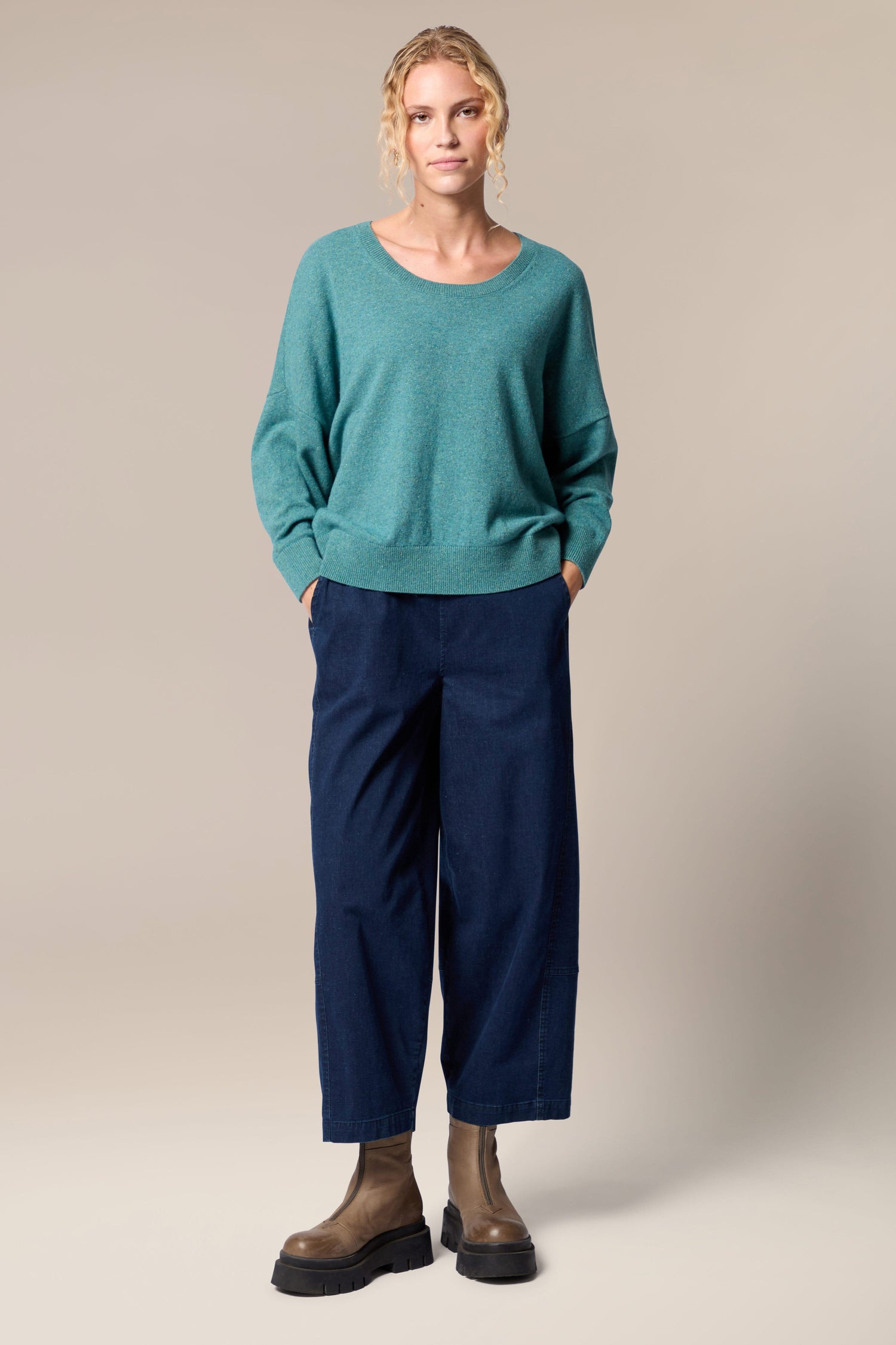 The model is wearing a Granit Scoop Knit sweater and navy trousers.