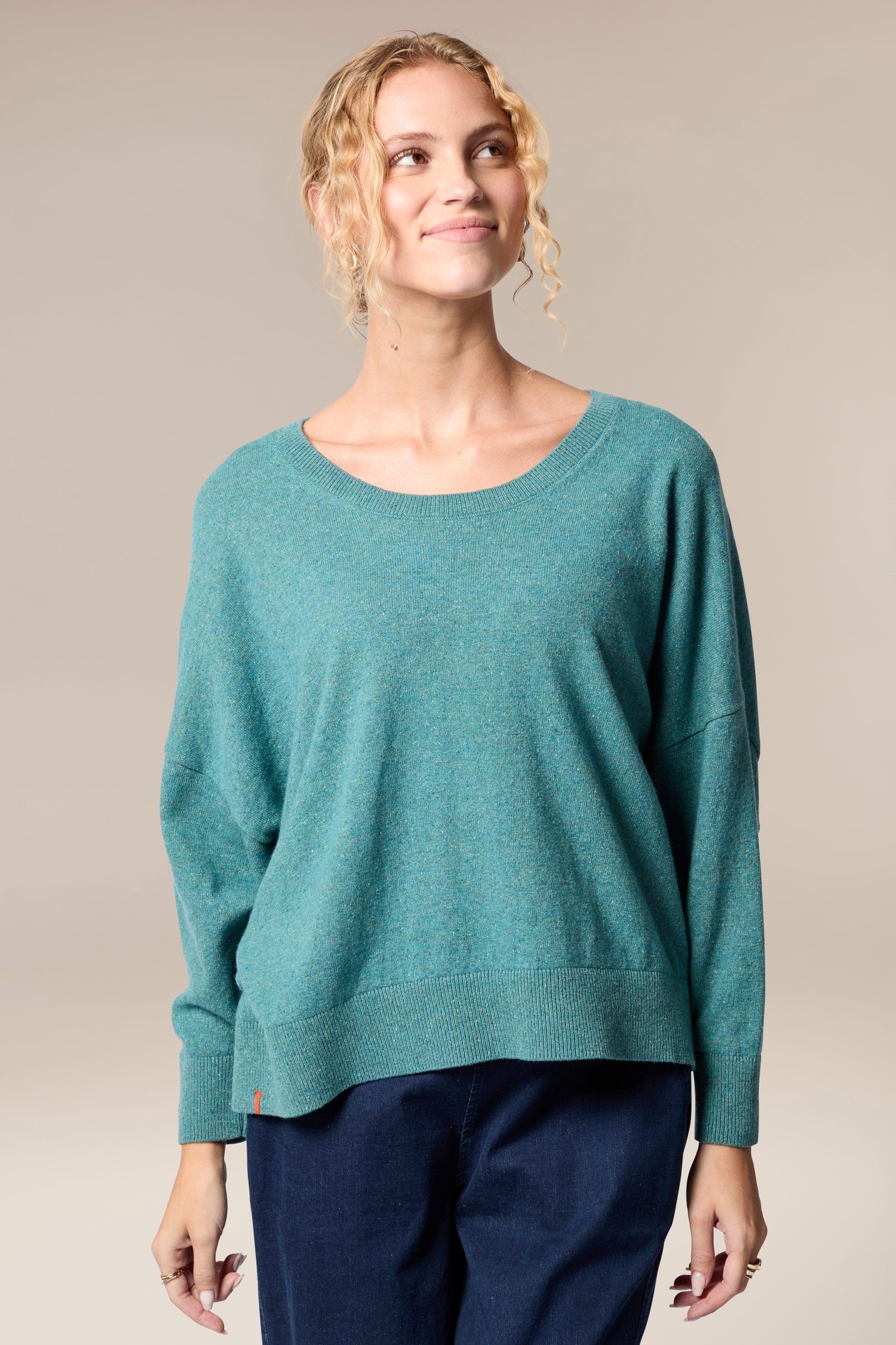 A woman wearing a Granit Scoop Knit sweater and blue pants showcases a sense of movement with her stylish attire.