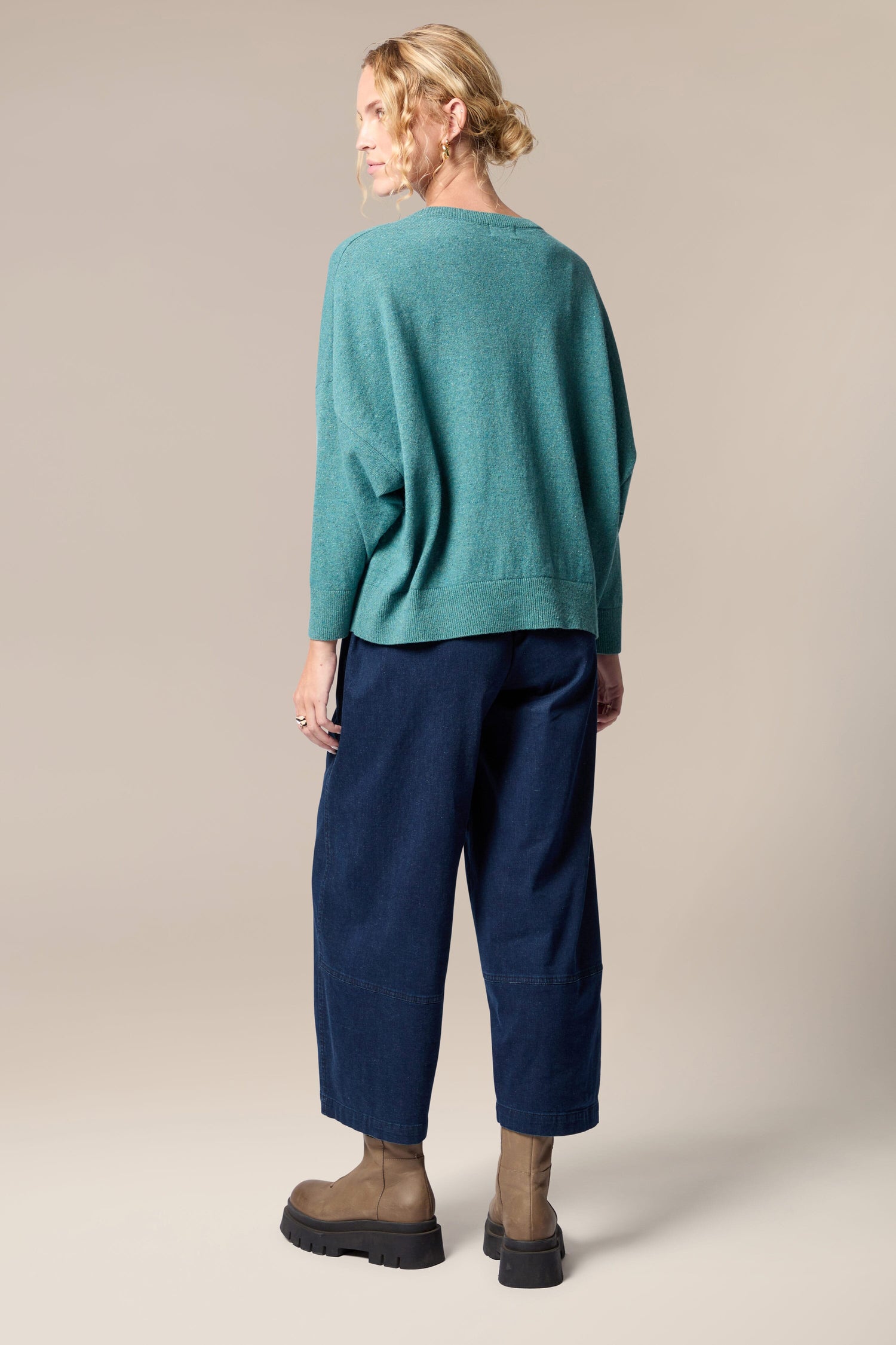 The woman exudes a sense of movement in her Granit Scoop Knit sweater, perfectly paired with blue pants.