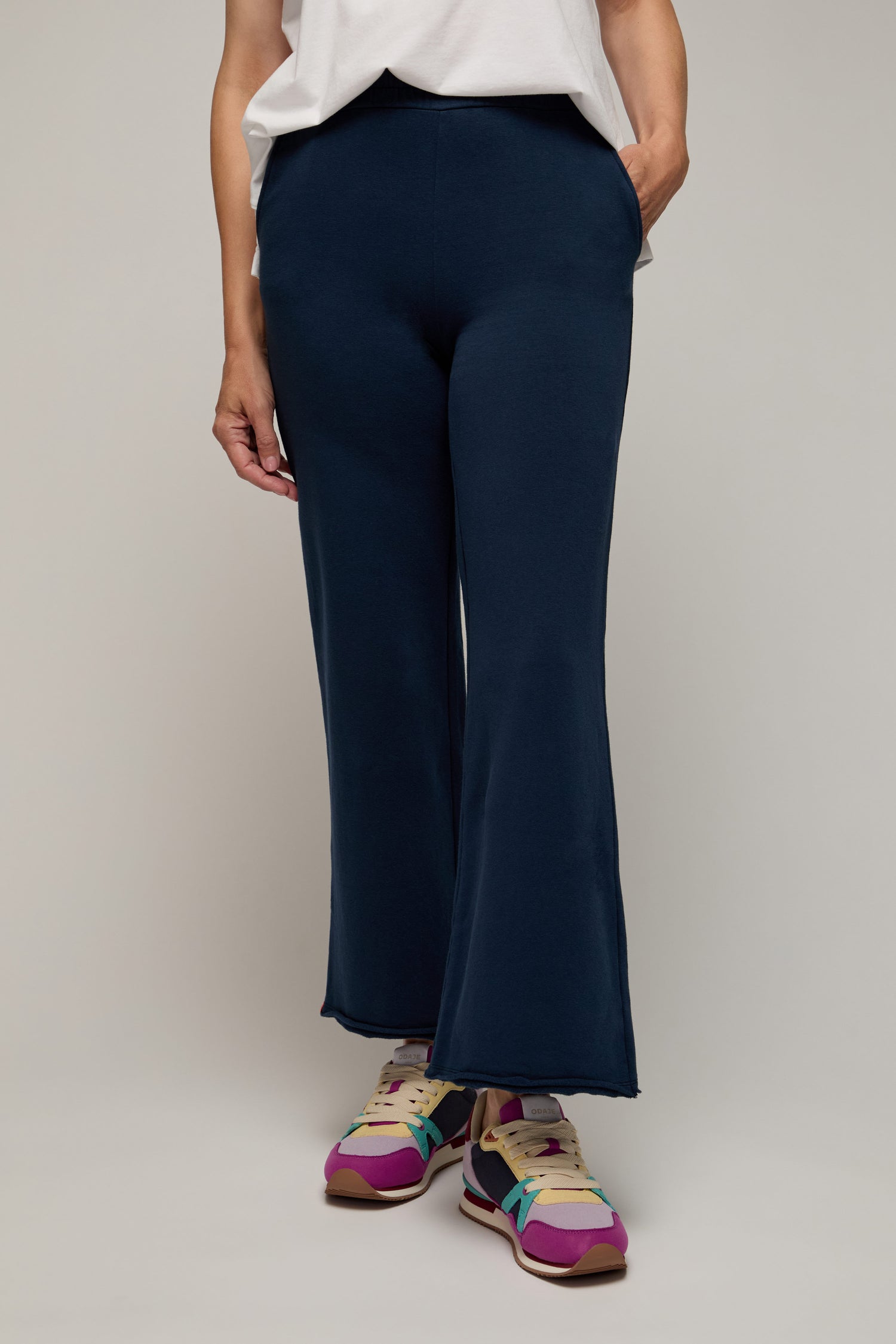 Person wearing the navy blue Lana Pant, featuring an elasticated waist, paired with a white top and colorful sneakers—ideal for elevated lounging—stands casually with one hand in their pocket against a neutral background.