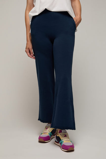 Person wearing the navy blue Lana Pant, featuring an elasticated waist, paired with a white top and colorful sneakers—ideal for elevated lounging—stands casually with one hand in their pocket against a neutral background.