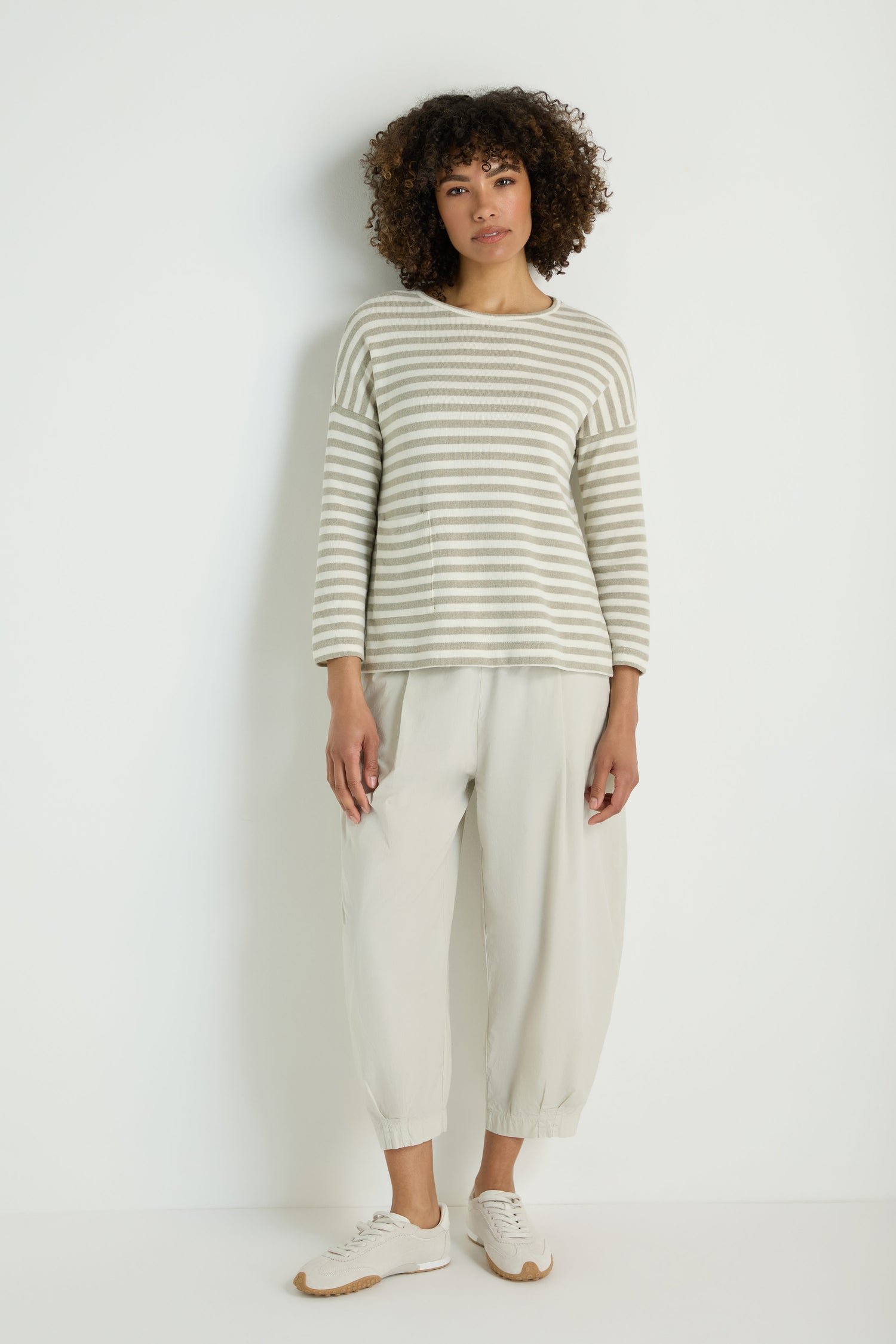 A person with curly hair wears the Stripe Pocket Fleece Top, light loose-fitting pants, and white sneakers, standing against a plain white background.