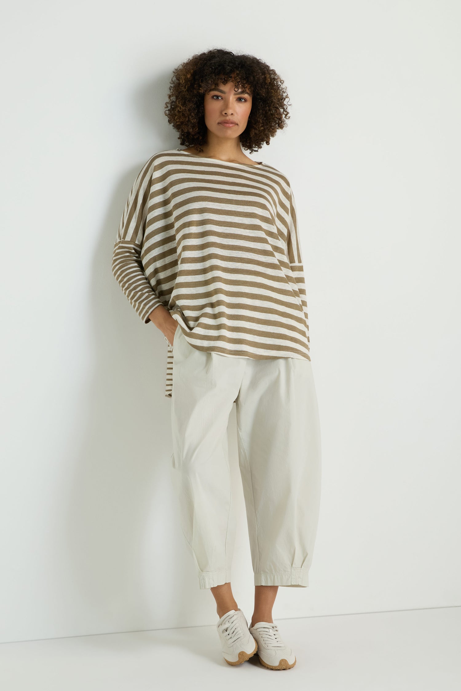 A person stands against a white wall wearing the Oversize Stripe Tunic, paired with loose white pants and white sneakers.