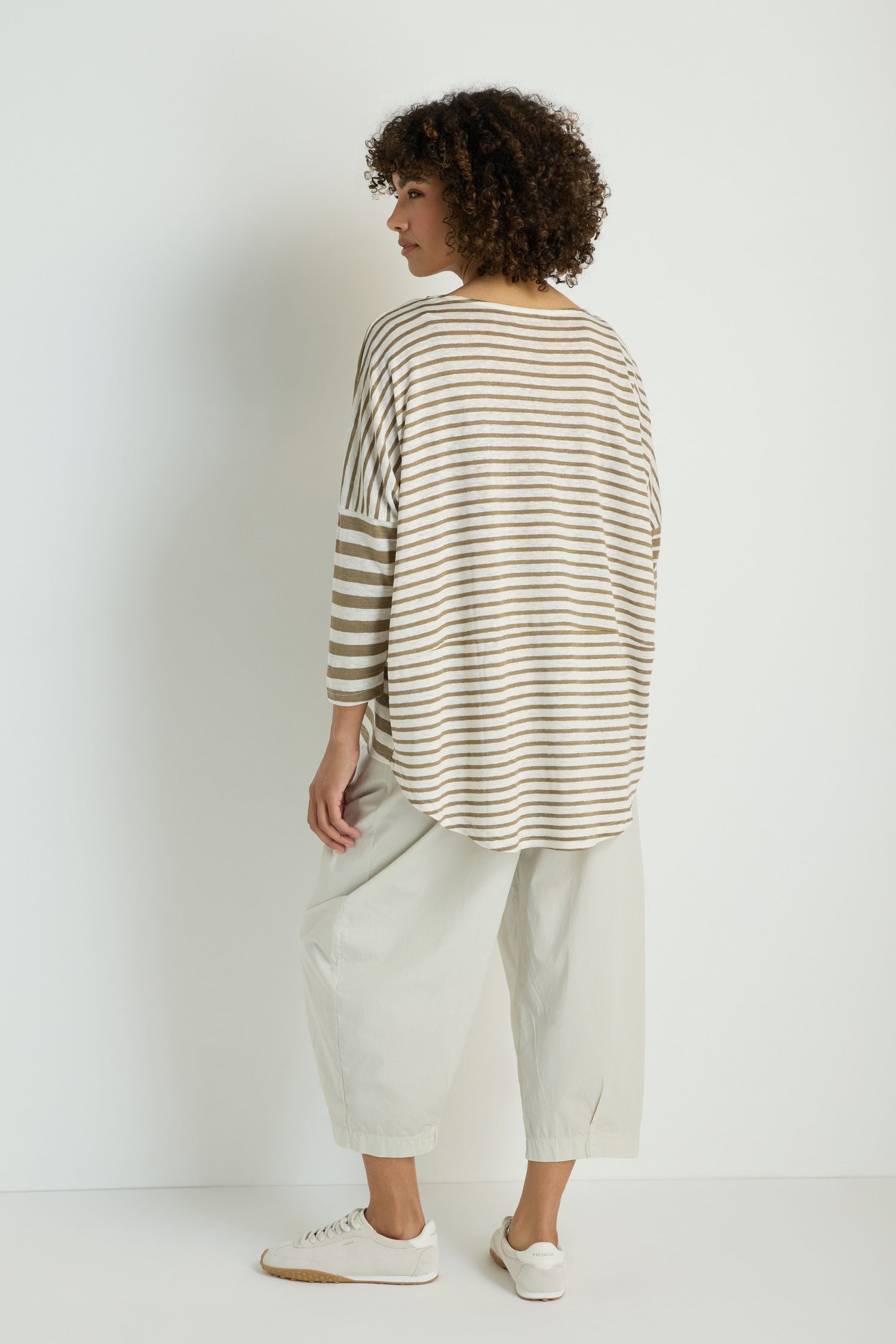A person stands against a white wall, facing away, wearing the Oversize Stripe Tunic with light-colored wide-leg pants and white sneakers.