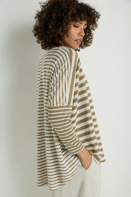 A person stands sideways against a plain background wearing the Oversize Stripe Tunic in beige and white with light-colored pants.