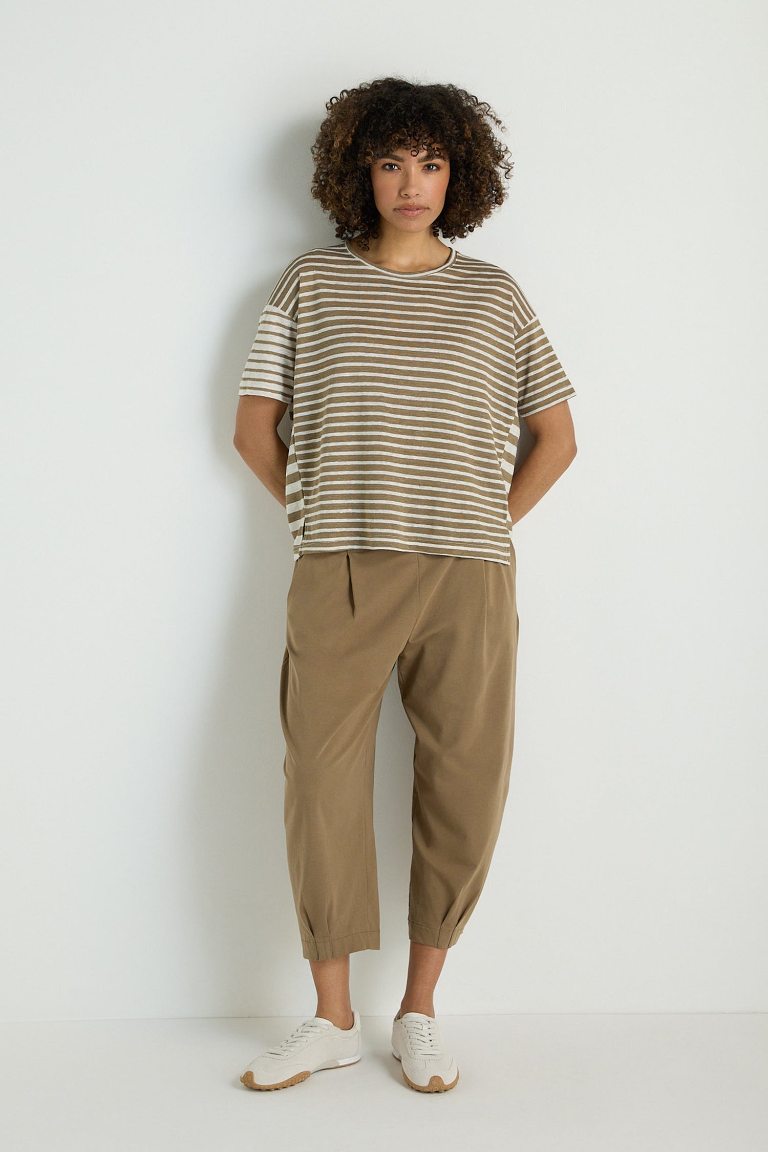 A person stands against a plain background, hands in pockets, wearing the Mixed Stripe T-Shirt made from a linen and viscose blend, tan cropped pants, and white sneakers.