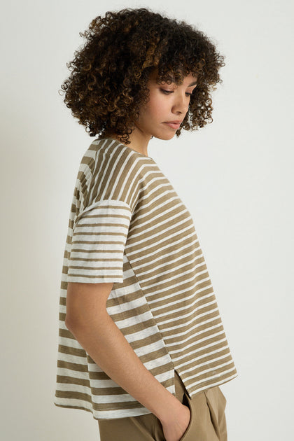 Person with curly hair stands in profile against a plain background, wearing the Mixed Stripe T-Shirt in beige and white with beige pants.