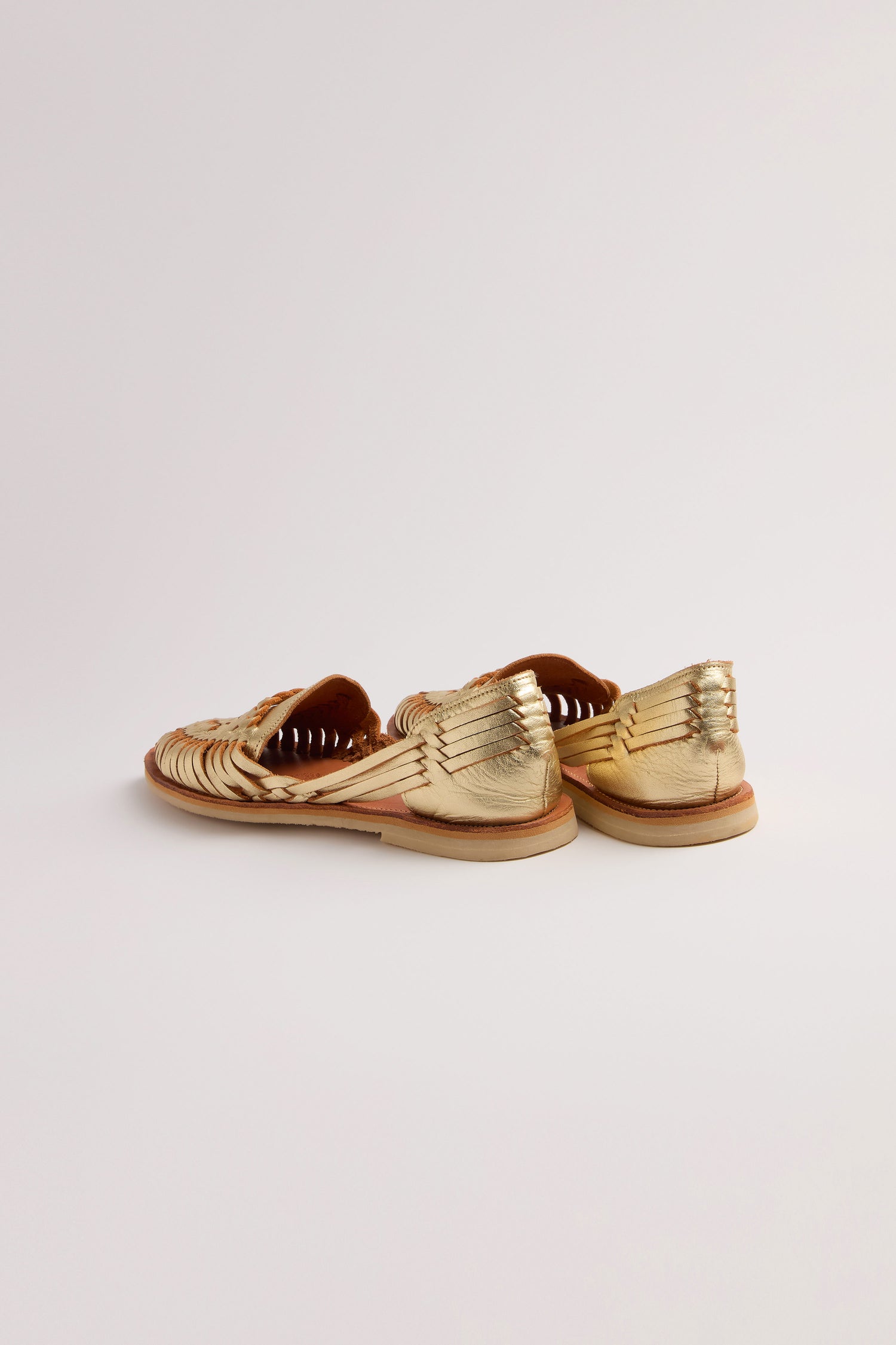 A pair of Alegre Leather Huarache Sandals with woven gold, flat soles, reminiscent of handcrafted designs from Mexico, is viewed from the back on a plain white surface.