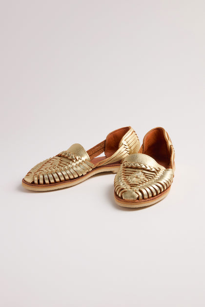 A pair of Alegre Leather Huarache Sandals, handcrafted in Mexico from exquisite gold woven leather, rests elegantly on a plain white background, offering breathable comfort with every step.