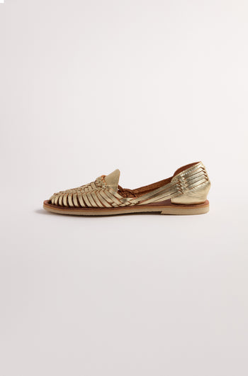 The Gold Alegre Leather Huarache Sandal by Mapache, handcrafted in Mexico, features woven leather straps and a flat sole, shown against a plain white background.
