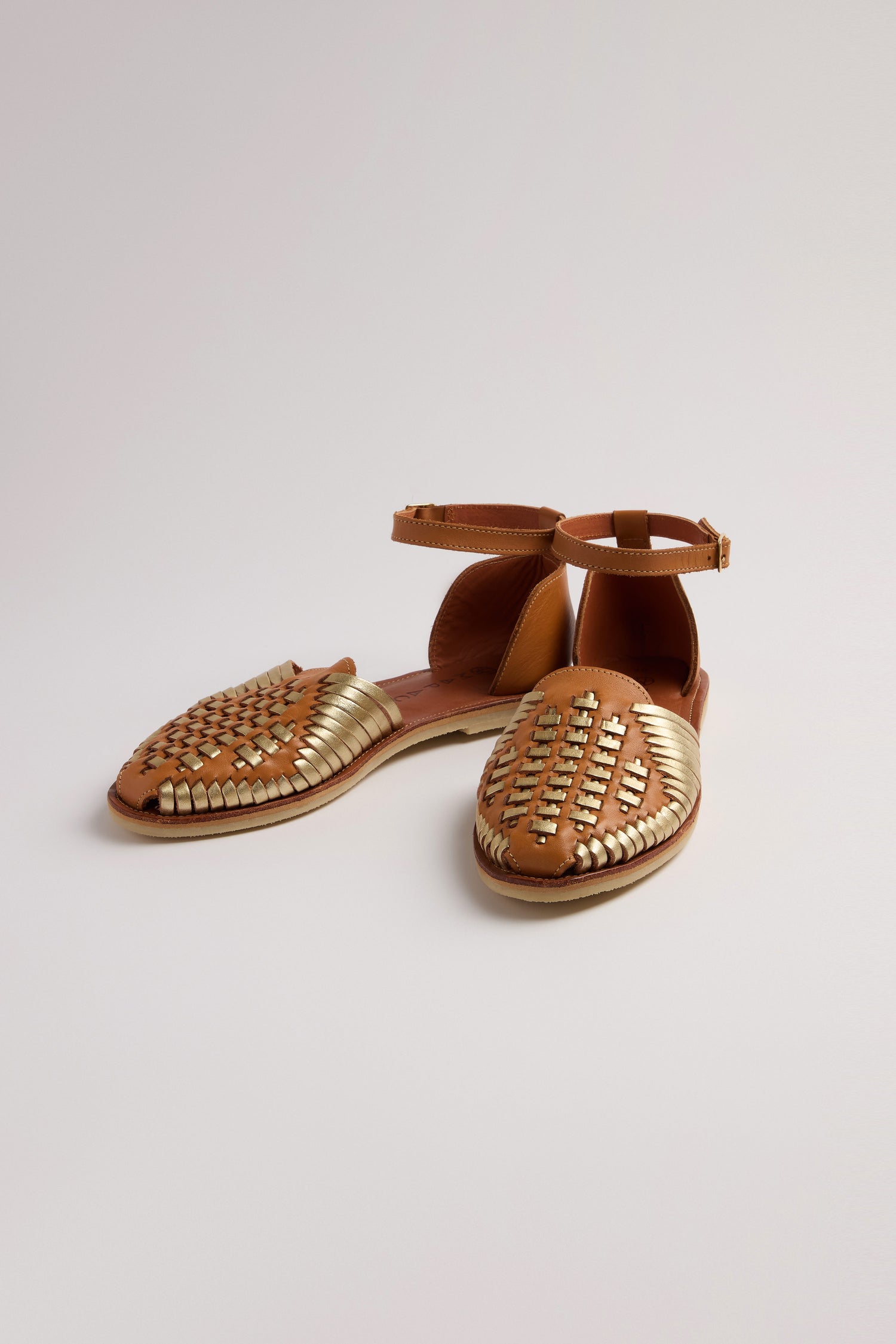 Camila Two Tone Leather Sandals feature woven designs with metallic accents and ankle straps, set against a plain brown background.