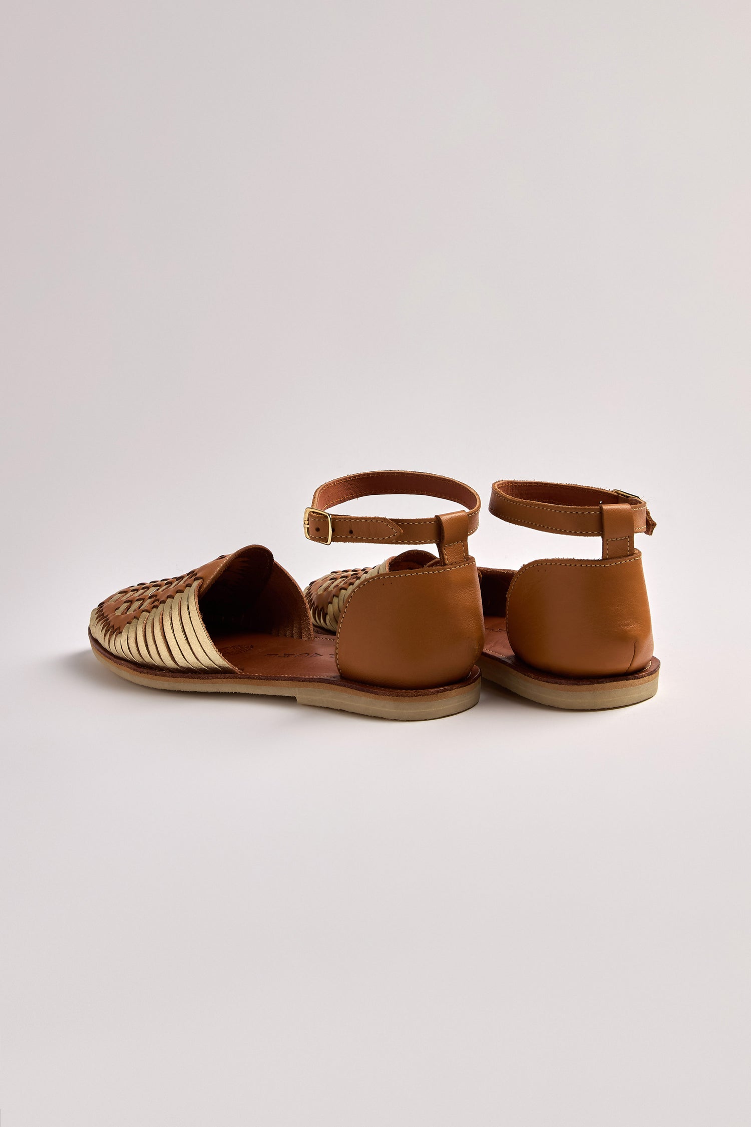 The Camila Two Tone Leather Sandals, made with brown and beige woven leather, showcase a chic design featuring ankle straps, elegantly set against a plain white background.