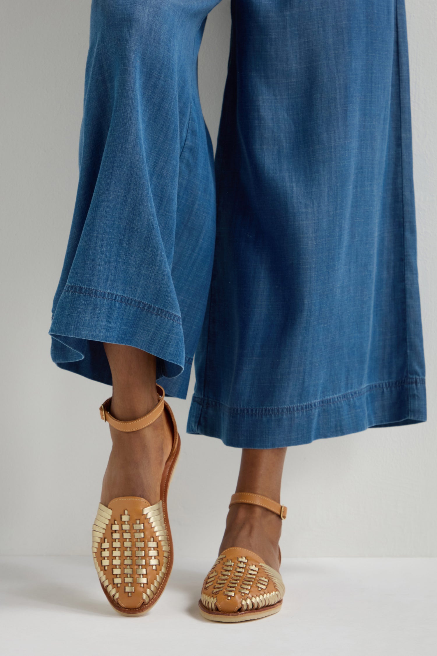 A person wearing wide-leg denim pants and Camila Two Tone Leather Sandals is standing on a light surface.