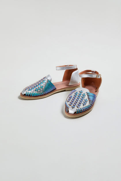 The Camila Mermaid Woven Sandals feature metallic blue and silver woven uppers, tan soles, and silver ankle straps. This online exclusive pair is shown on a plain white background.