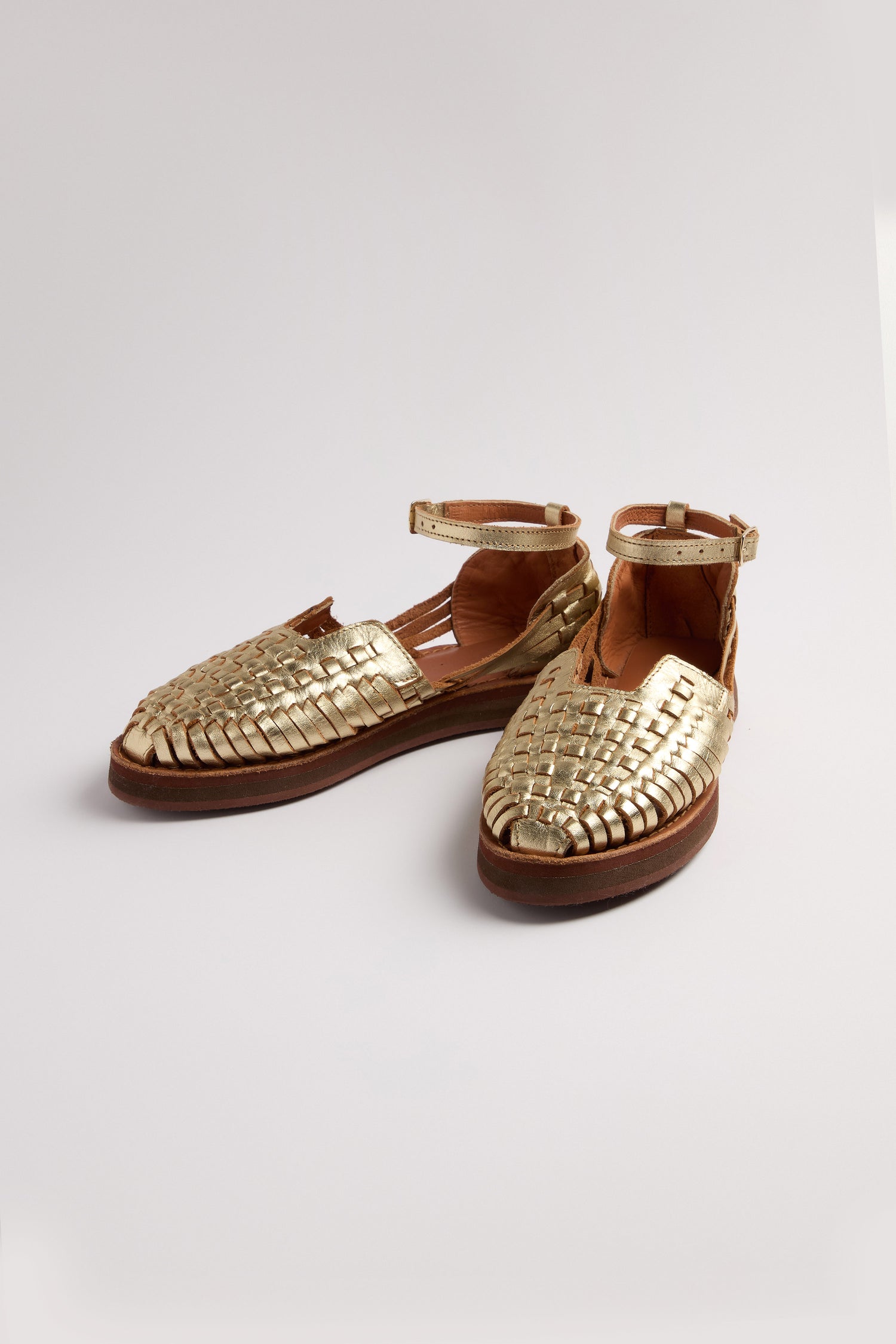 The Carmen Platform Woven Leather Sandals are handcrafted in Mexico, featuring gold woven leather with closed toes and ankle straps, set against a plain light background.