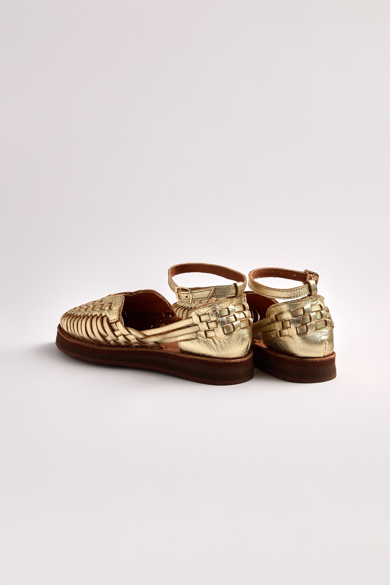 Two Carmen Platform Woven Leather Sandals, handcrafted in Mexico with gold woven leather, feature platform soles and ankle straps, viewed from the back against a plain white background.