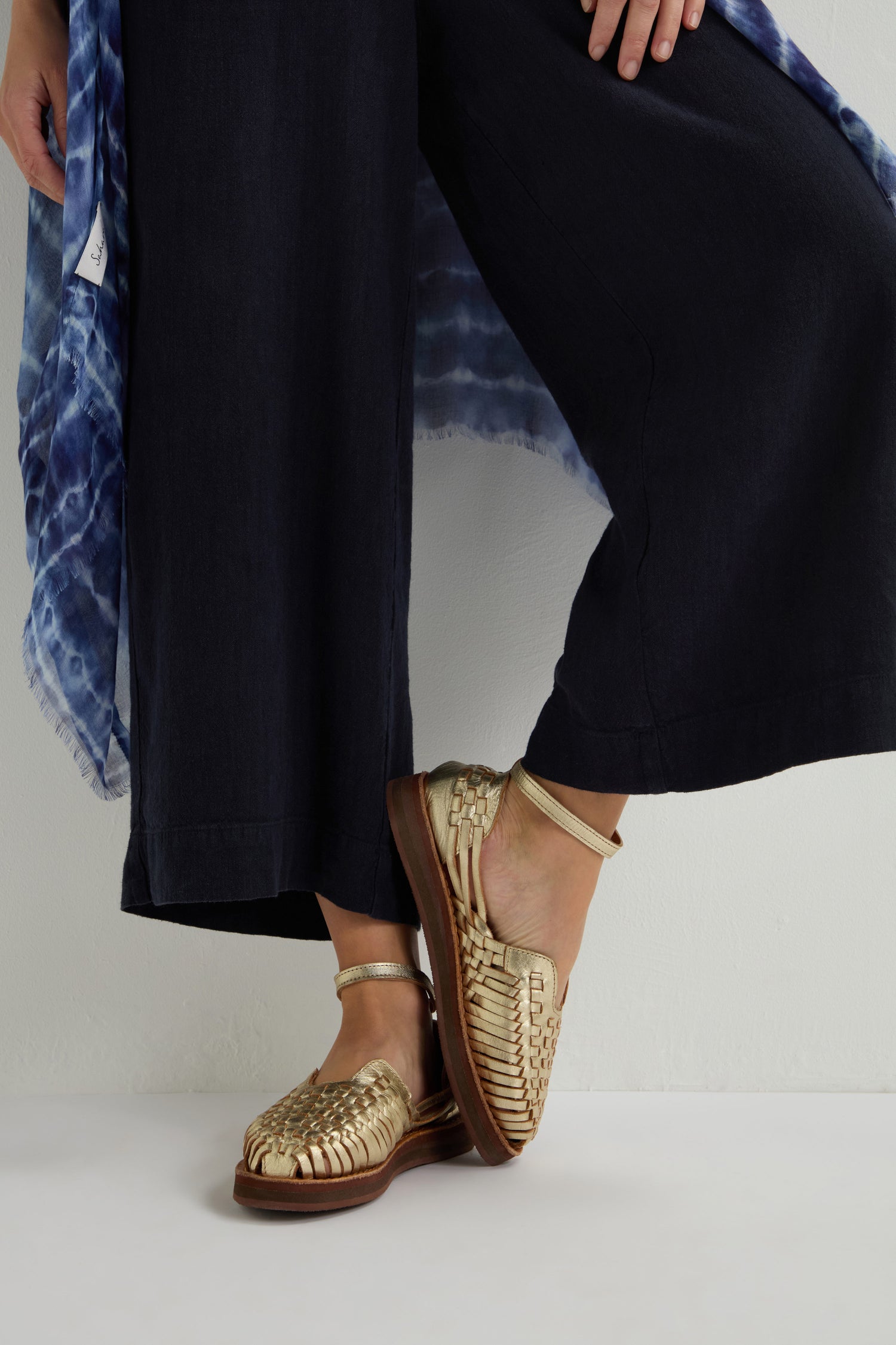 A person stylishly wears Carmen Platform Woven Leather Sandals with black wide-leg pants and a beautifully blue patterned garment.