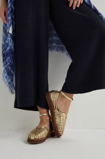 A person stylishly wears Carmen Platform Woven Leather Sandals with black wide-leg pants and a beautifully blue patterned garment.