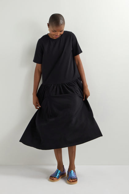 A person in a black dress and Frida Woven Leather Sandals, handcrafted in Mexico, stands against a plain white background, looking down.