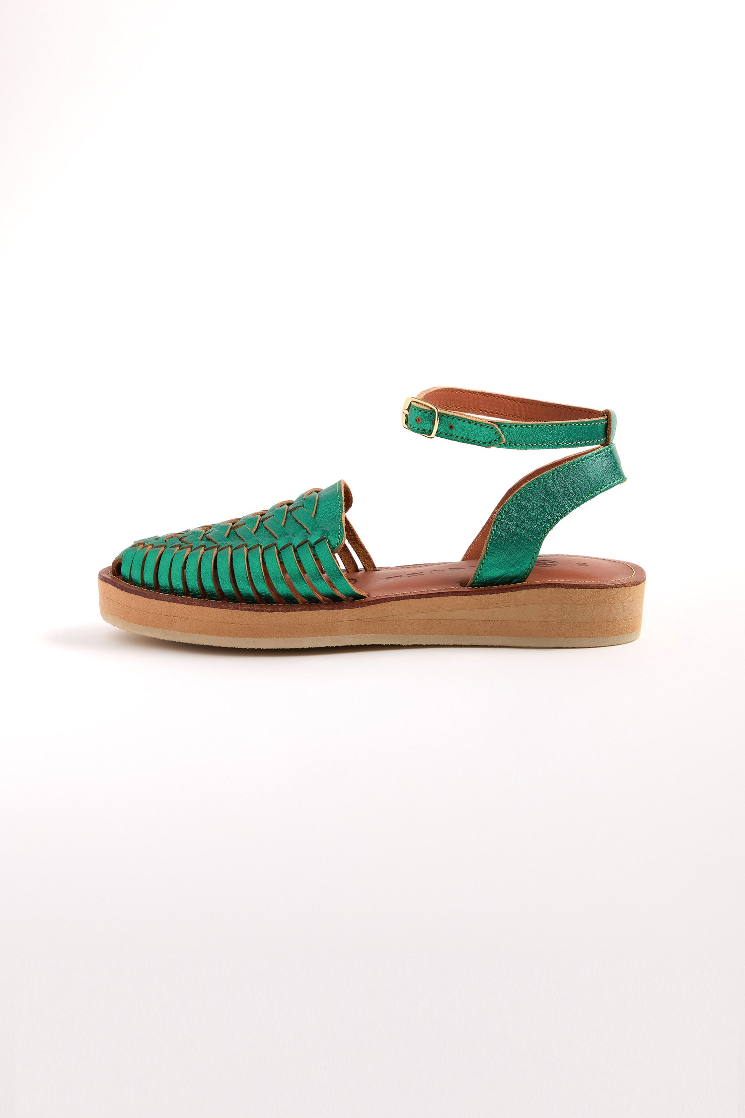 The Loma Platform Braided Leather Sandals feature a green woven leather upper, flat beige sole, and adjustable ankle strap in a side view, offering a perfect blend of style and tradition in handcrafted fashion.