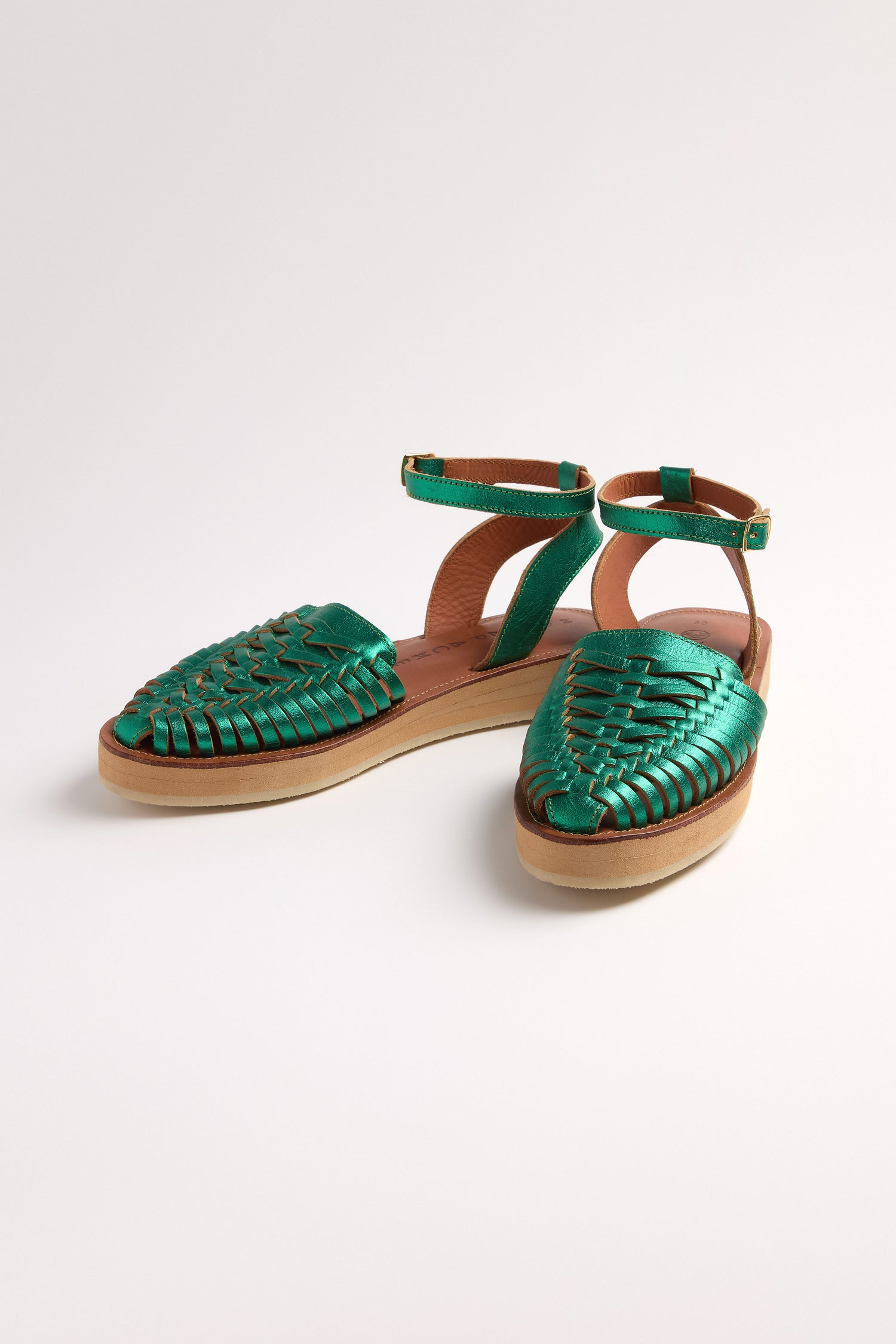 The Loma Platform Braided Leather Sandals, in green with ankle straps and flat soles, are beautifully showcased on a white background, highlighting the artistry of handcrafted leather footwear.