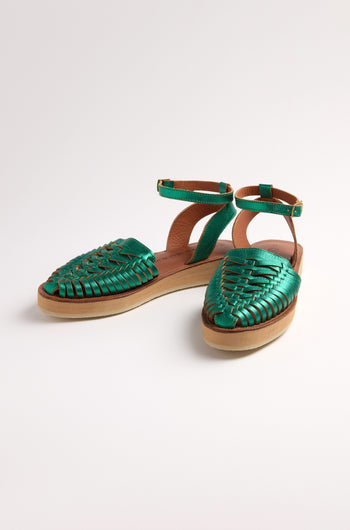 The Loma Platform Braided Leather Sandals, in green with ankle straps and flat soles, are beautifully showcased on a white background, highlighting the artistry of handcrafted leather footwear.