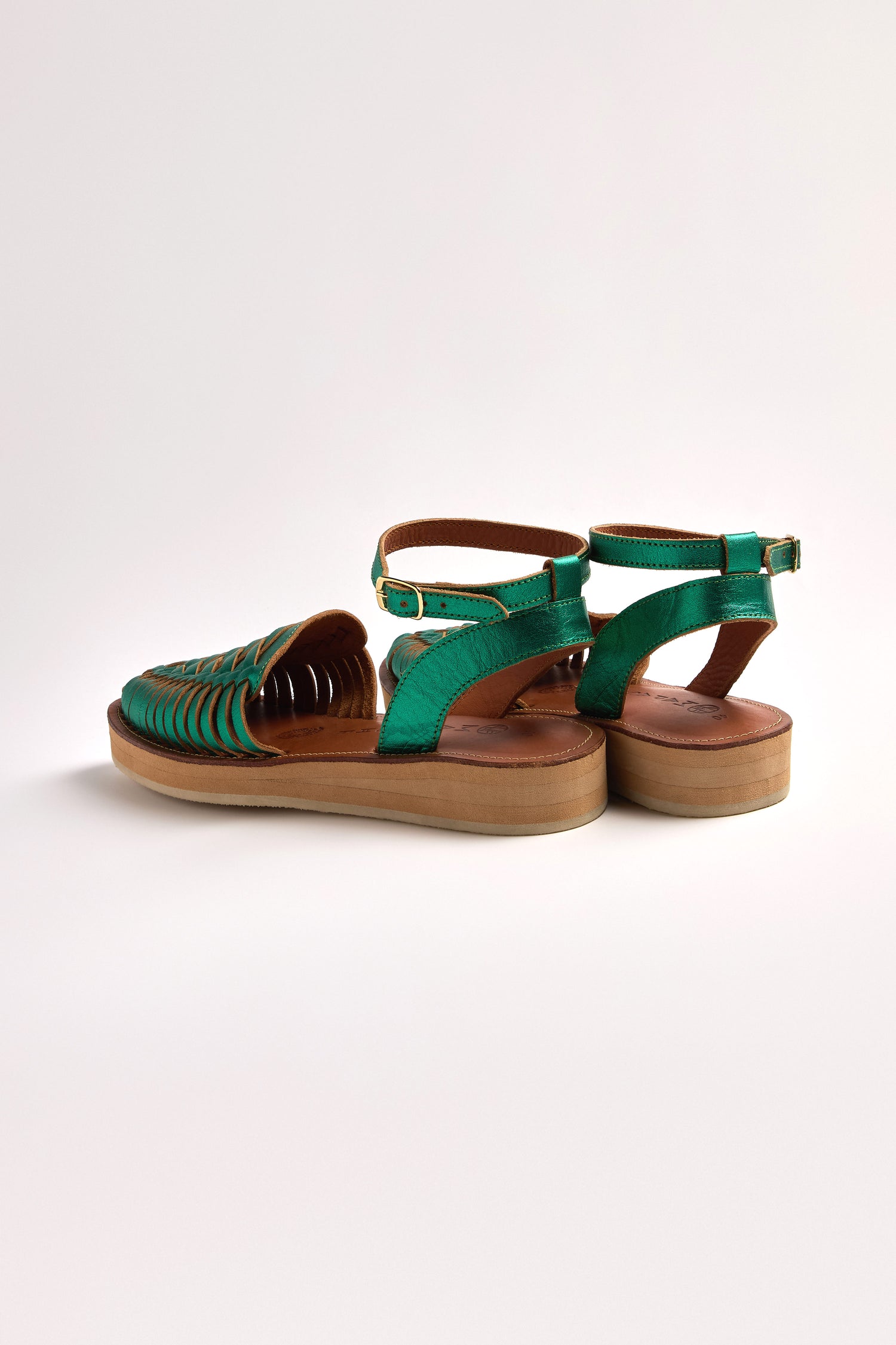 Explore the elegance of the Loma Platform Braided Leather Sandals, showcasing a green woven open-toe design and adjustable ankle straps against a neutral backdrop.