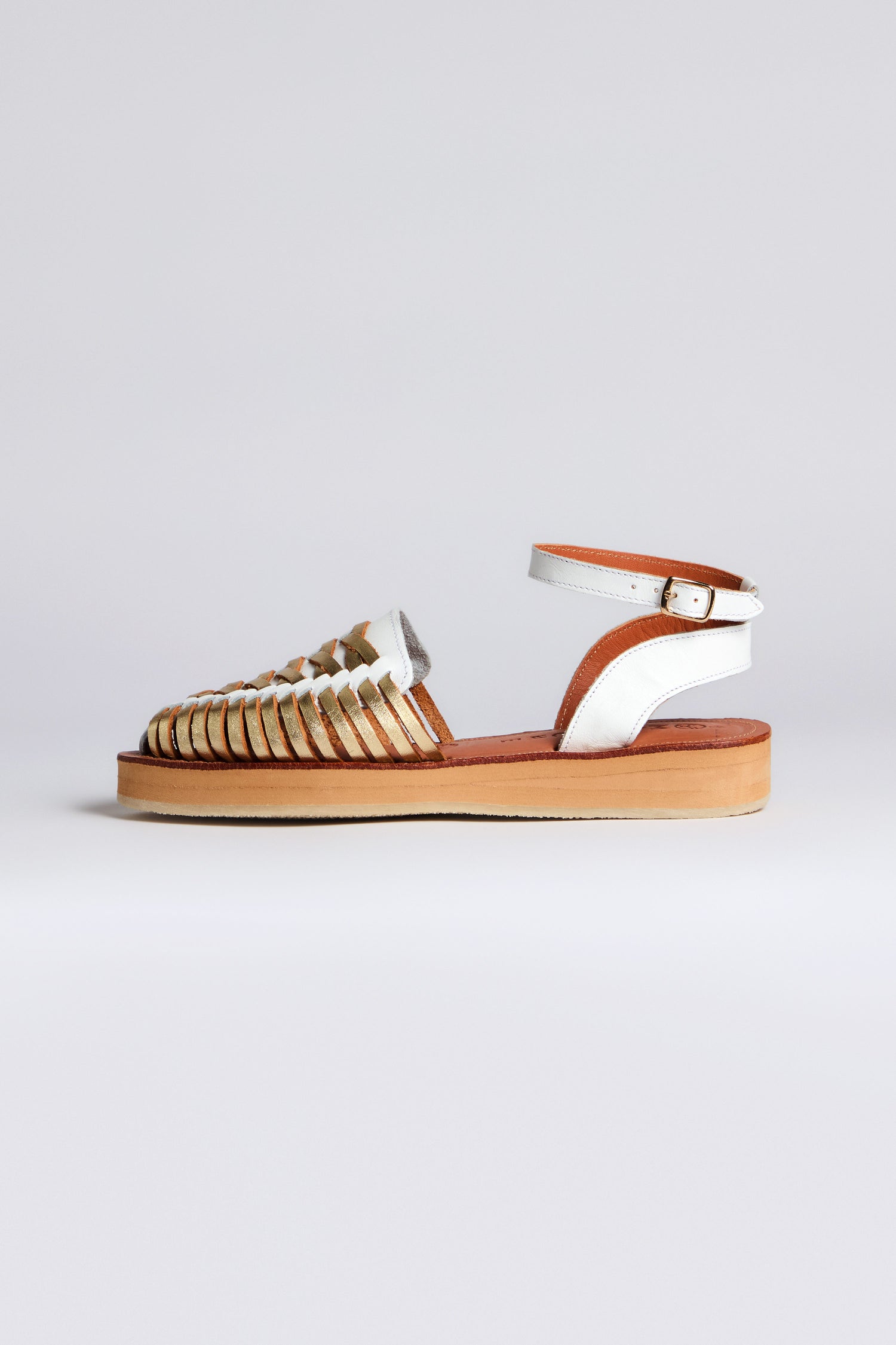 The Loma Platform Braided Leather Sandals showcase a white and brown woven closed toe and ankle strap on a tan sole. This handcrafted piece is elegantly displayed against a plain white background, embodying the Mapache signature style.