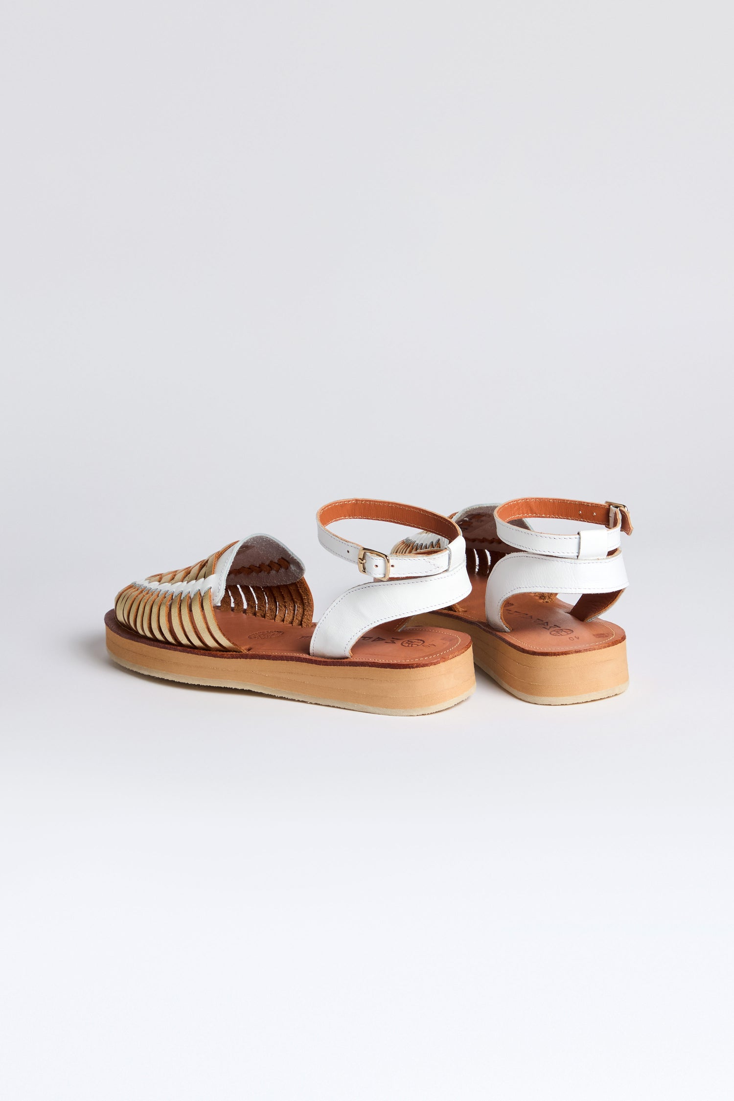 The Loma Platform Braided Leather Sandals feature a woven beige front and sleek white ankle straps, perfect for light backdrops. Crafted with care, they blend style and comfort seamlessly.