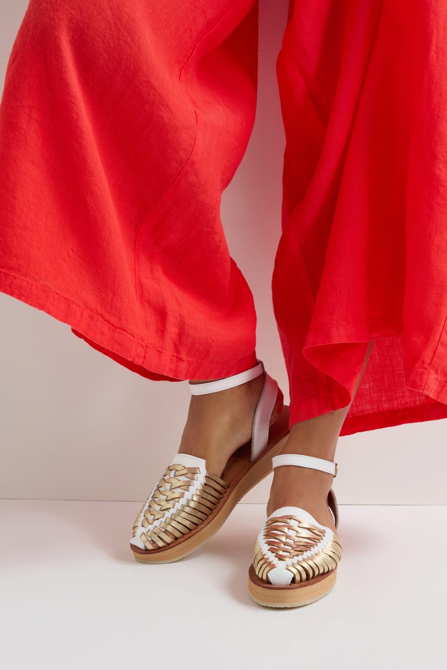 A person in red pants wears Loma Platform Braided Leather Sandals with ankle straps, standing with slightly inward-pointing toes.