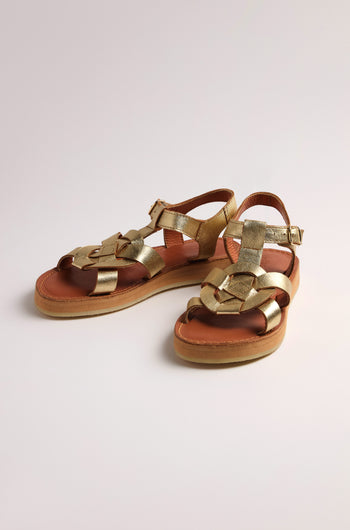 The Tulum Leather Buckle Sandals feature gold metallic woven straps, cushioned soles for comfort, tan leather soles, and handmade premium leather ankle buckles against a neutral background.