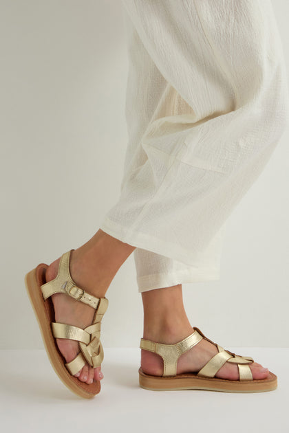 A person in cream-colored pants and Tulum Leather Buckle Sandals, made from premium handmade leather, stands on a light surface.