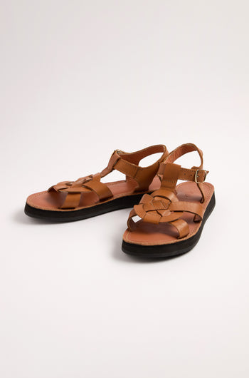 The Tulum Leather Buckle Sandals are handmade with premium brown leather, featuring straps, a buckle closure, cushioned for comfort, and black soles, elegantly placed on a light surface.